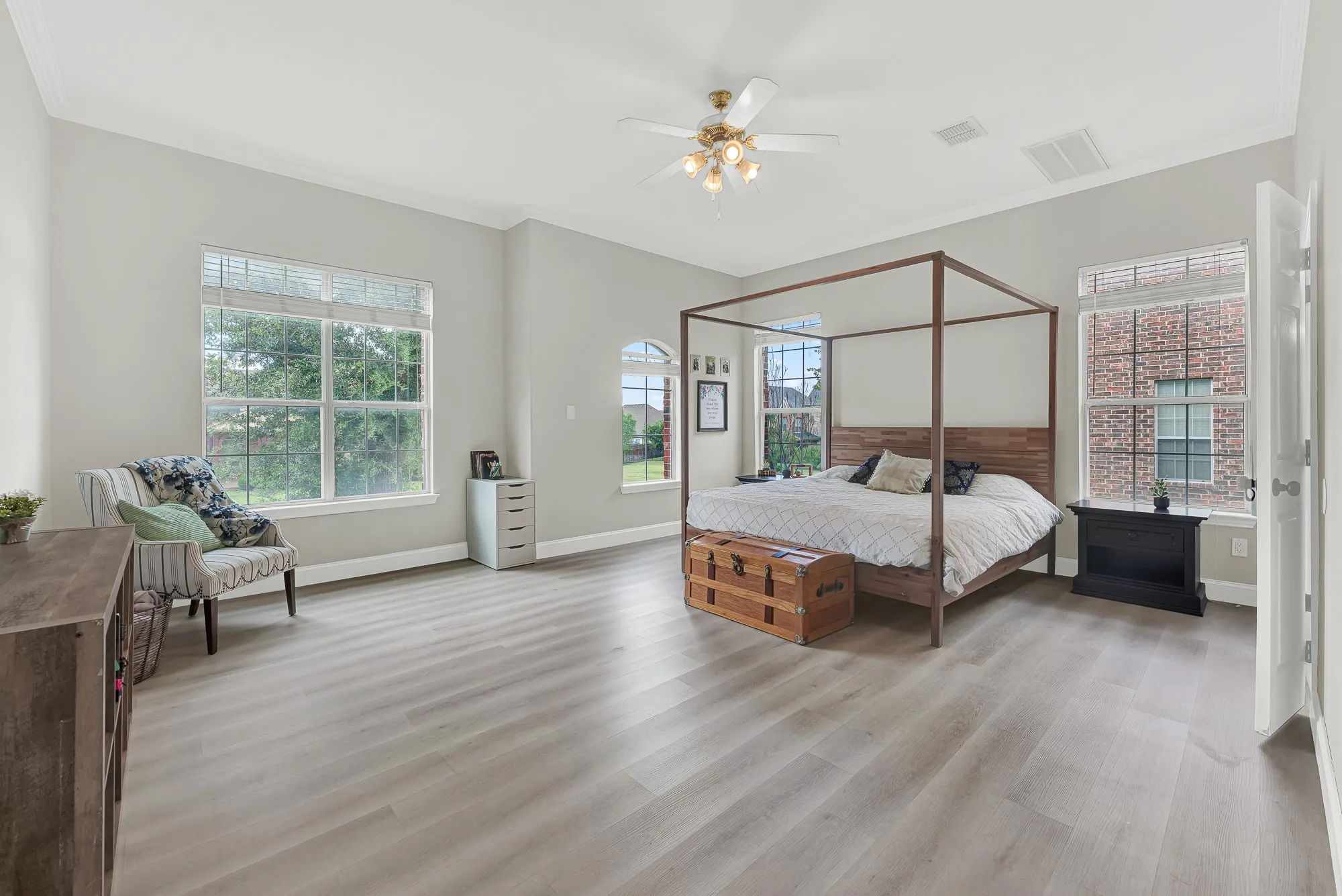 Spacious bedroom featuring light wood-finish flooring, multiple windows providing ample natural light, crown molding, and a ceiling fan with integrated lighting