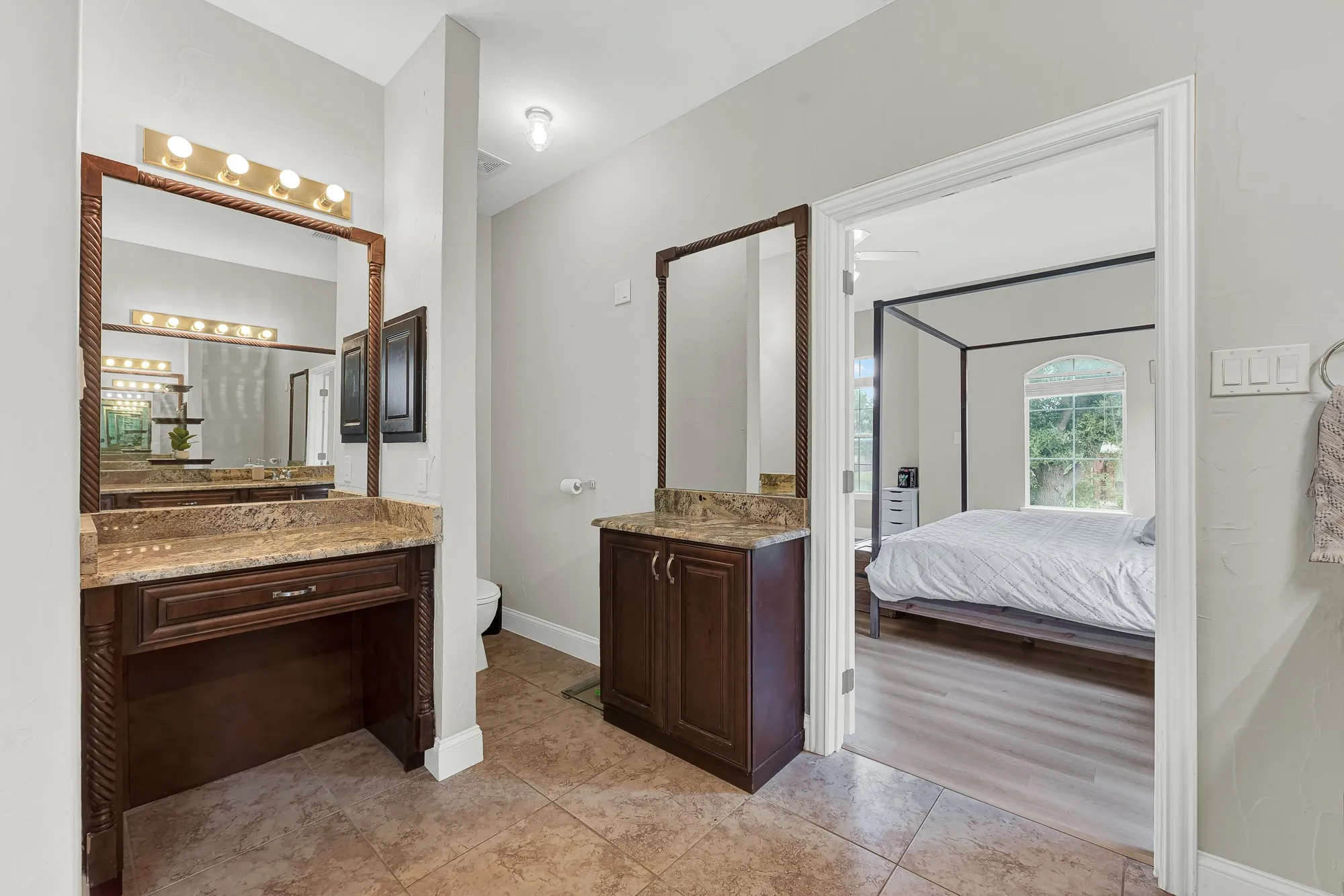 Vanity area featuring two dark wood cabinetry units, a dedicated makeup vanity, and two framed mirrors with integrated lighting