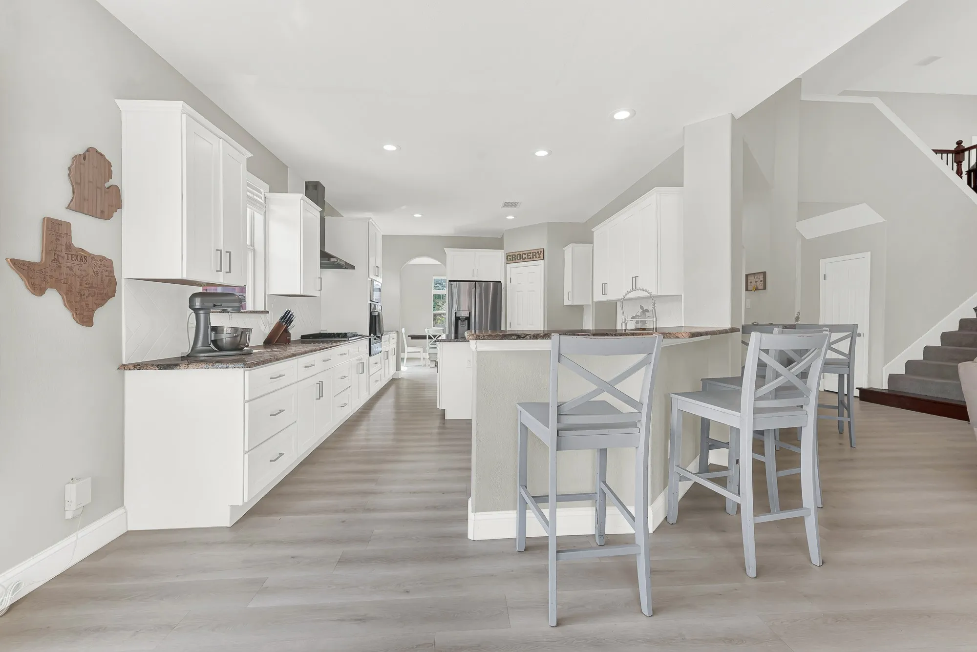 Open-concept kitchen featuring white cabinetry, stone countertops, a breakfast bar, recessed lighting, and wood-finish flooring