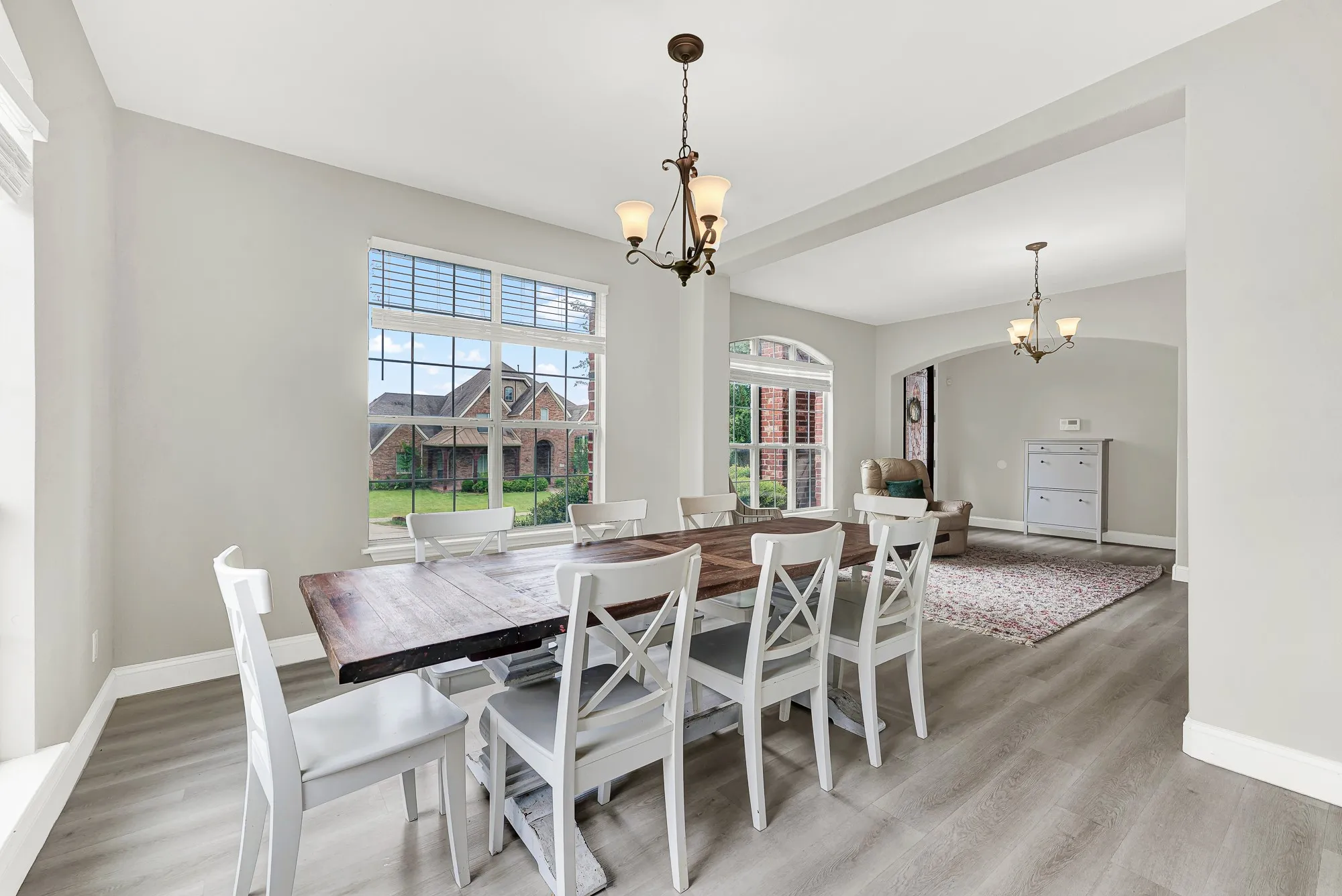 Dining area featuring wood-finish flooring, a contemporary chandelier, large windows with horizontal blinds, and an arched entry to an additional space