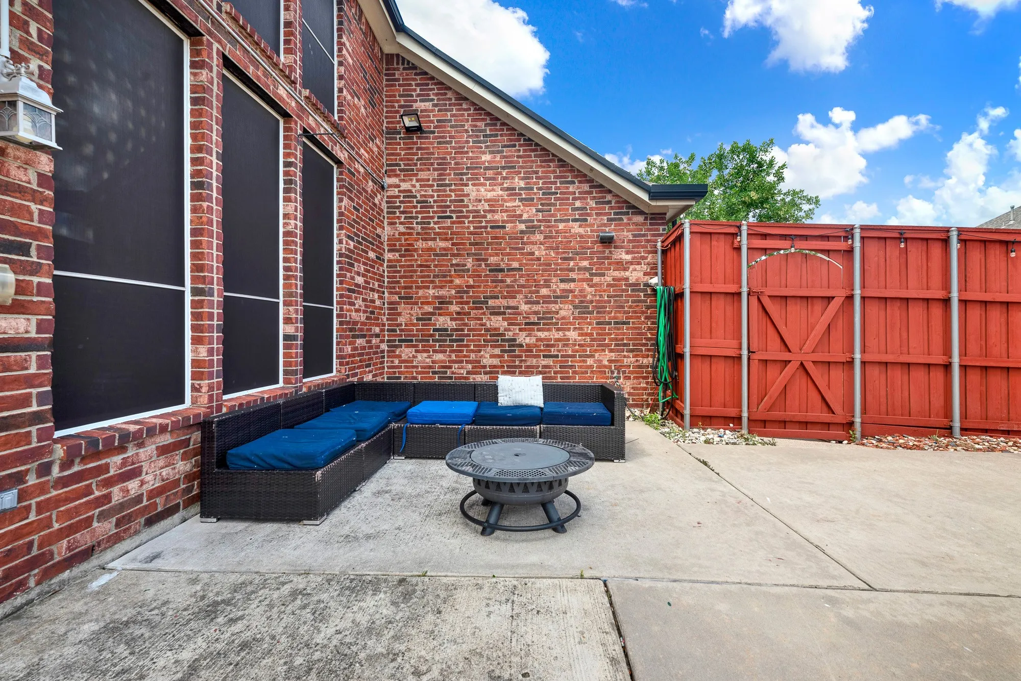 Spacious outdoor patio featuring a brick facade, privacy fence, and large concrete flooring