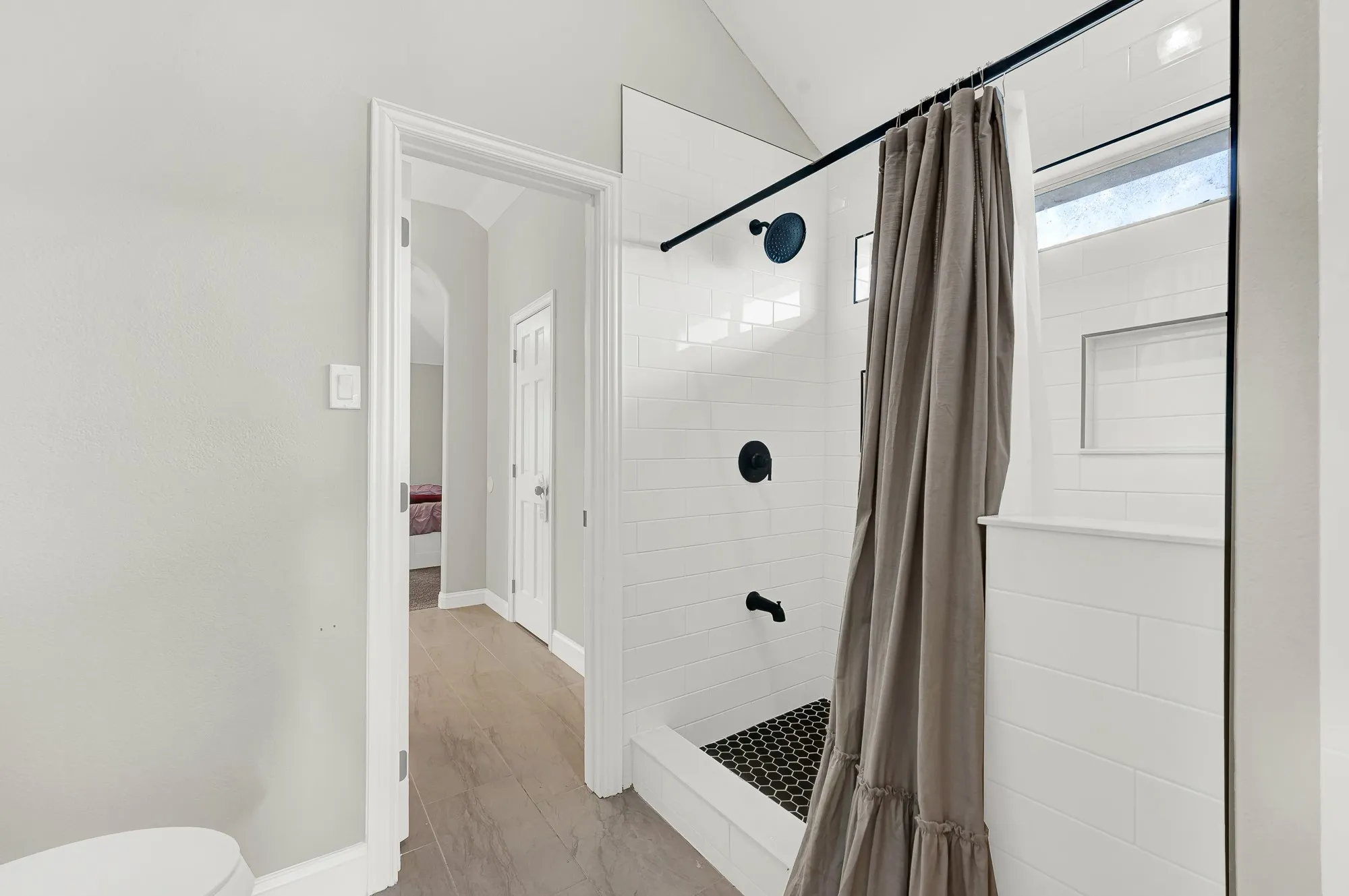Walk-in shower featuring subway tile walls, black hexagonal mosaic tile flooring, and matte black fixtures