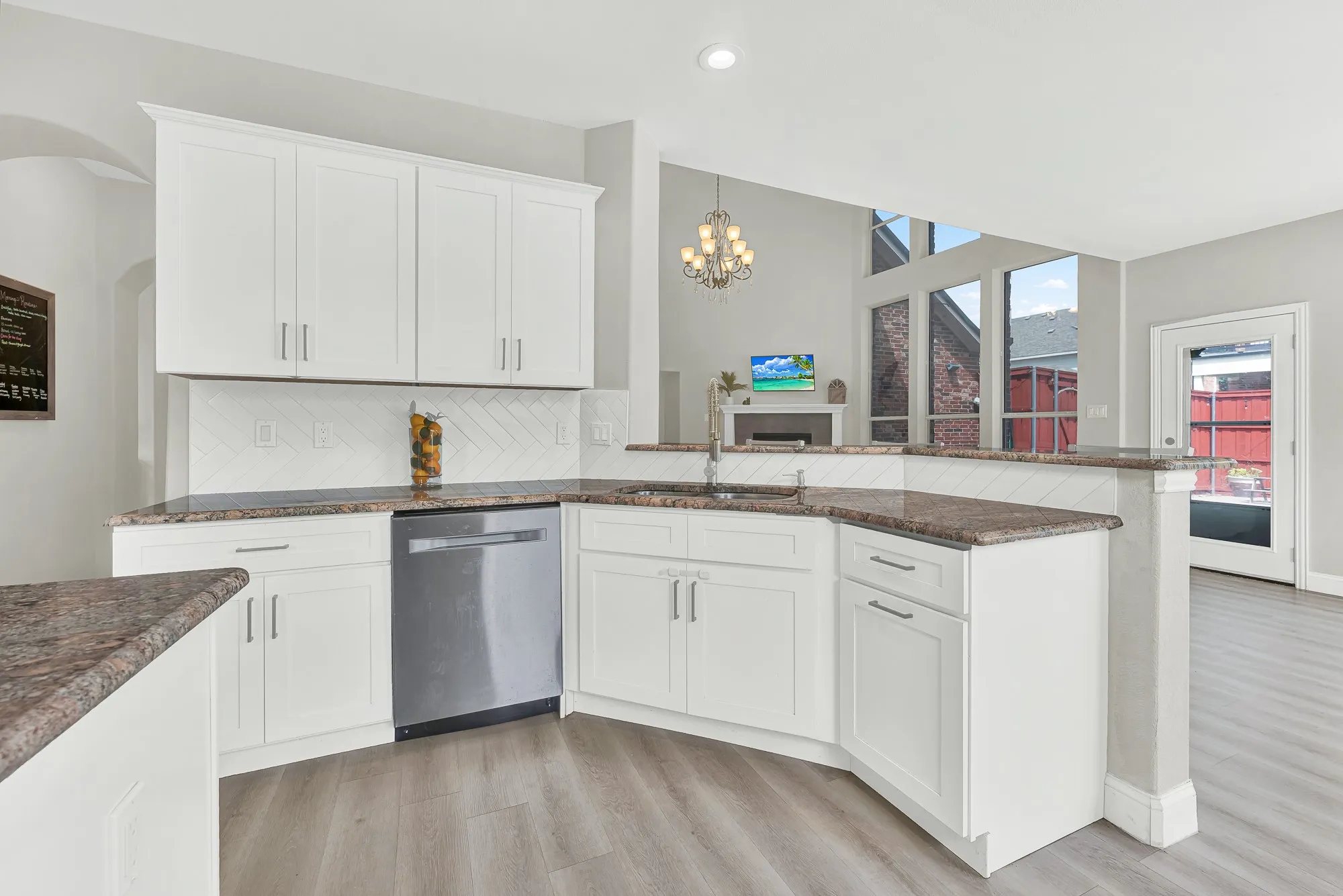 Kitchen featuring white cabinetry, stone countertops, stainless steel dishwasher, and a herringbone tile backsplash