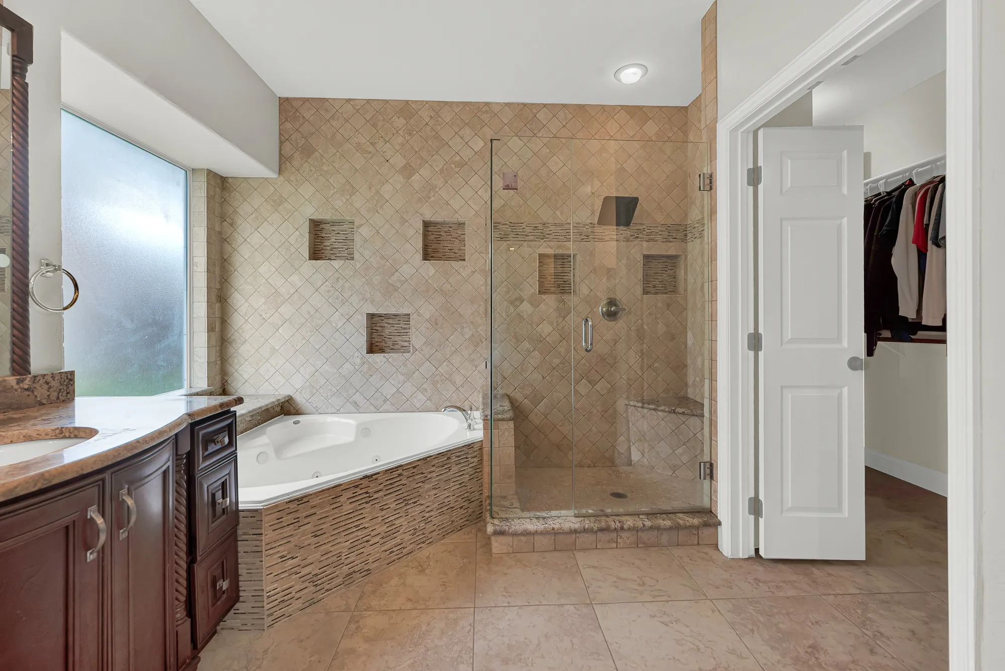 Bathroom featuring an angular jetted tub, a glass-enclosed shower with a built-in bench and recessed shelving, and a vanity with a stone countertop and double sinks