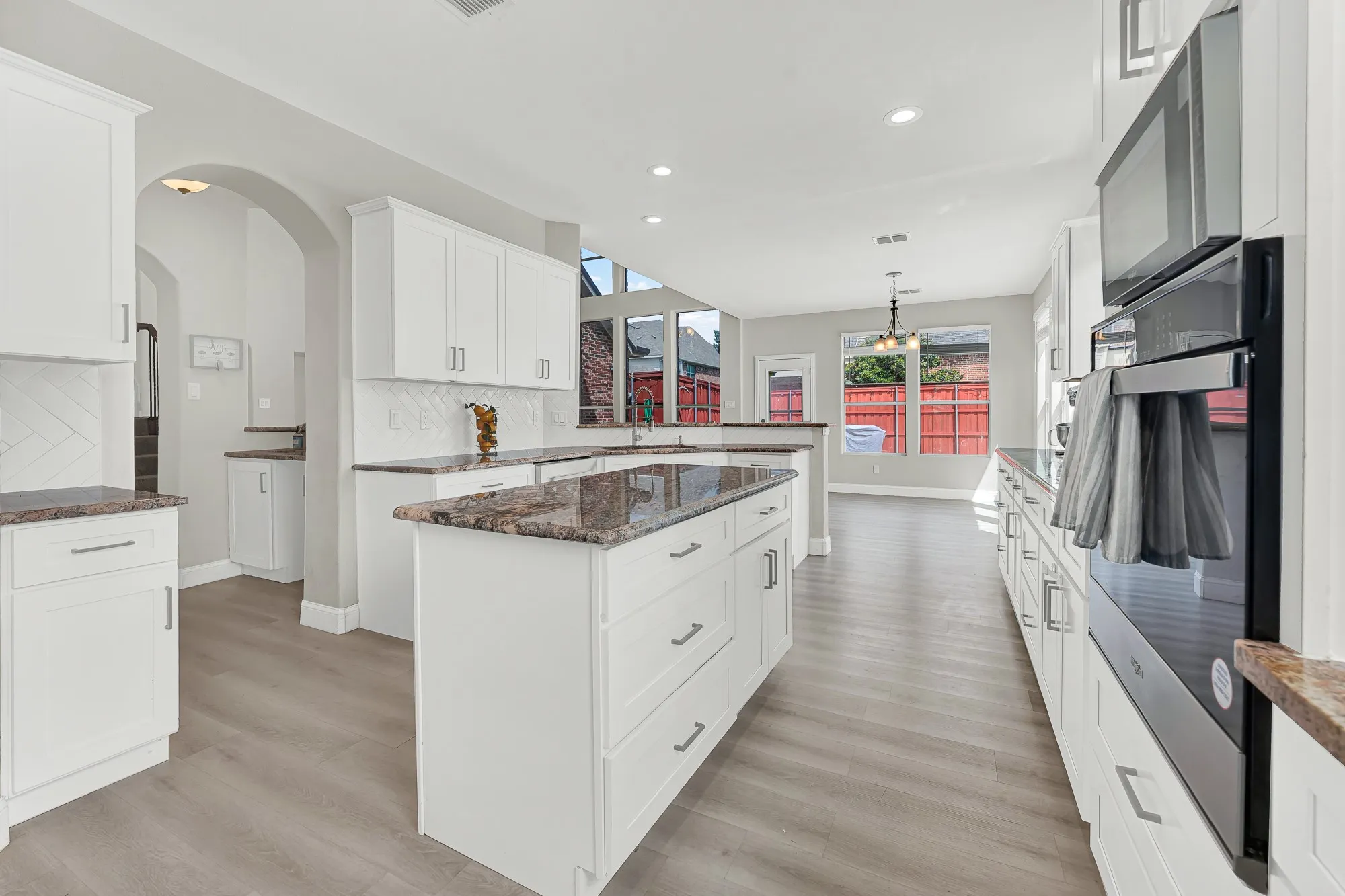 Spacious kitchen featuring an expansive center island with storage, white cabinetry, dark stone countertops, and wood-finish flooring