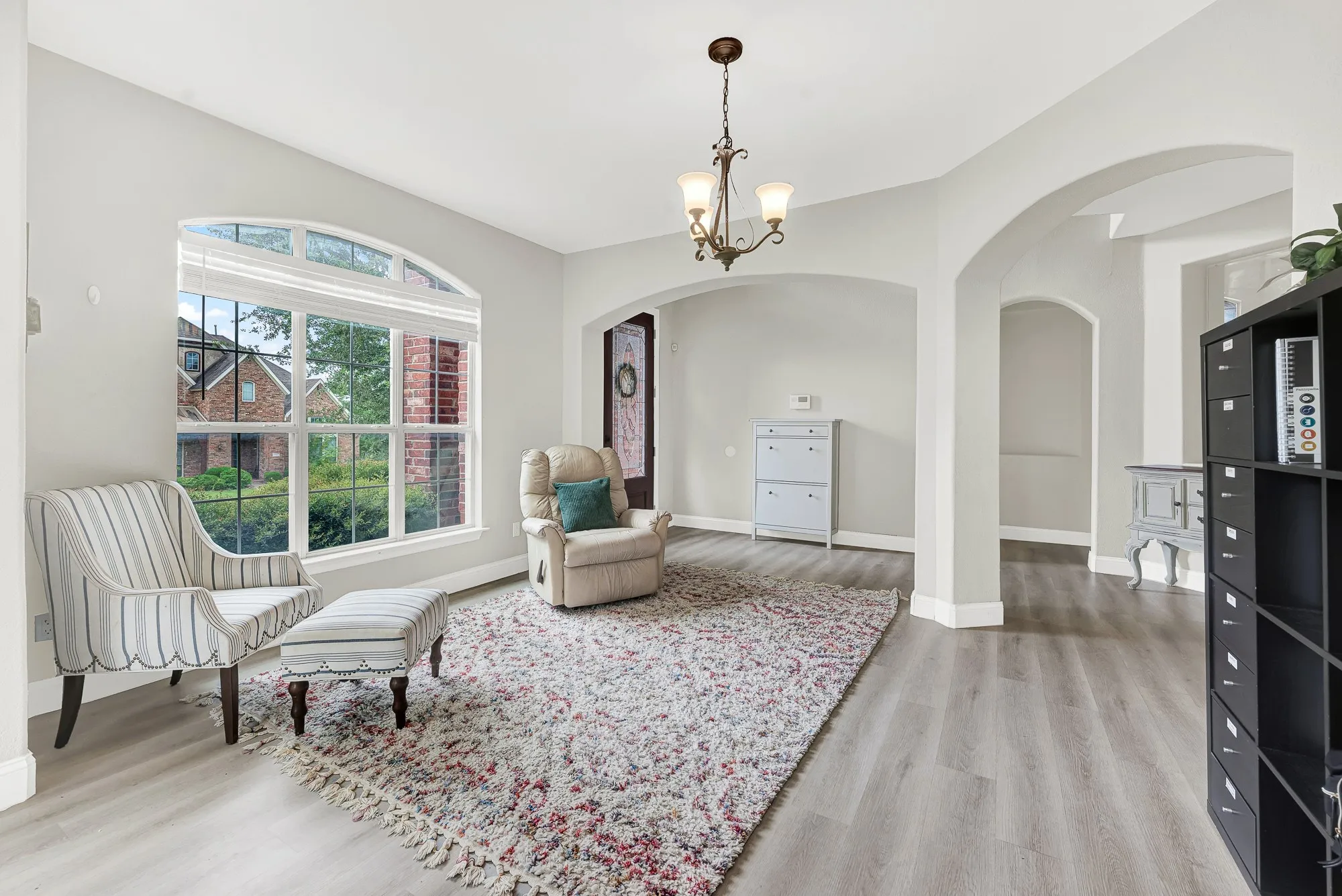 Bright interior space featuring an arched window with blinds, wood-finish flooring, and arched doorways