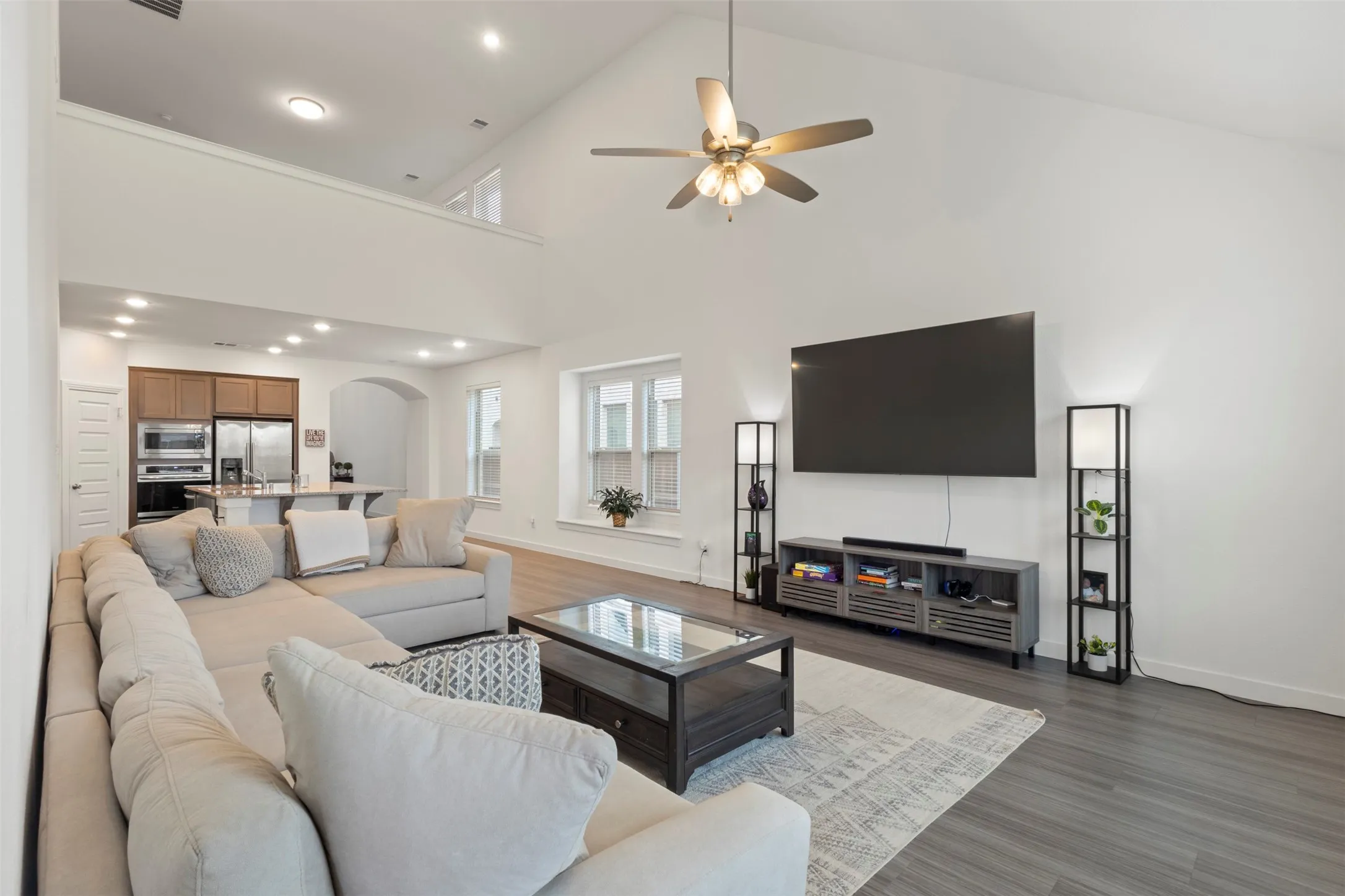 Living area featuring high vaulted ceiling, arched walkways, dark wood finished floors, a ceiling fan, and recessed lighting