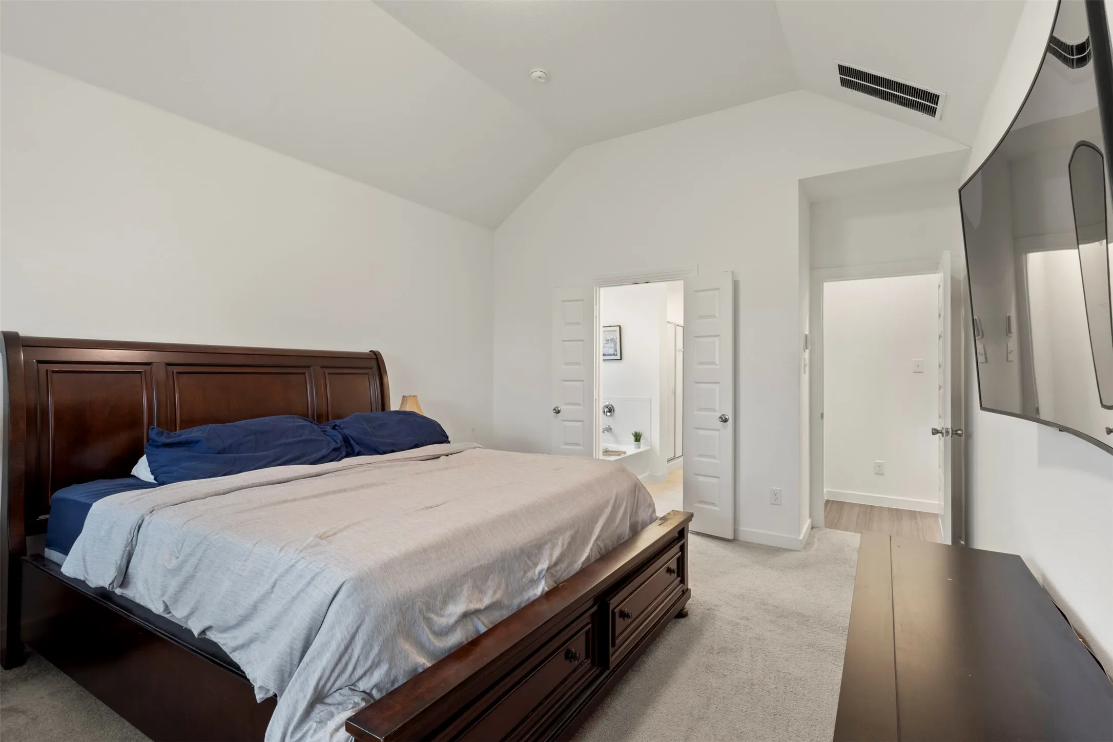 Bedroom with light carpet, ensuite bath, and lofted ceiling