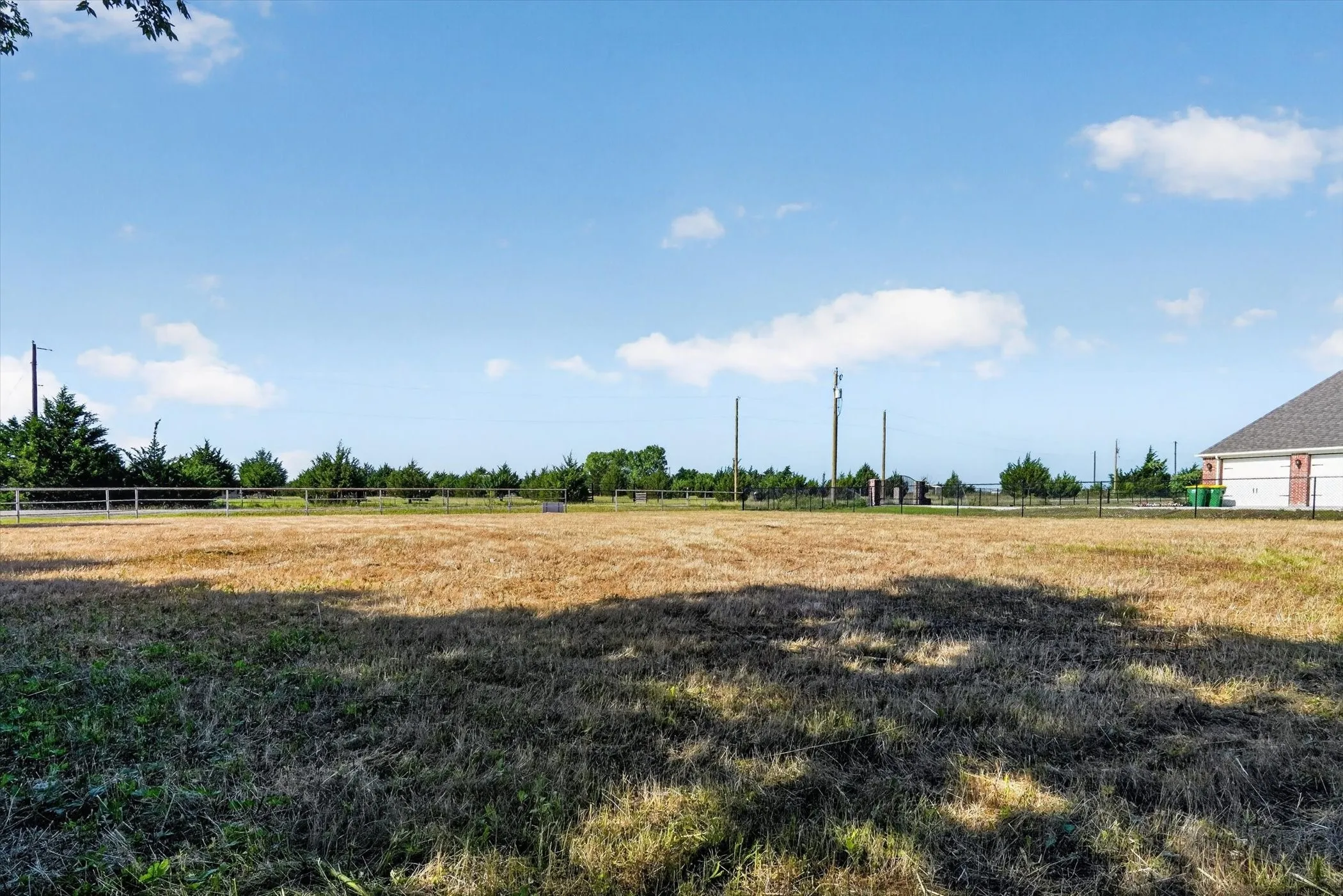 Expansive open lot featuring a clear sky, distant tree line, and partial brick-sided structure