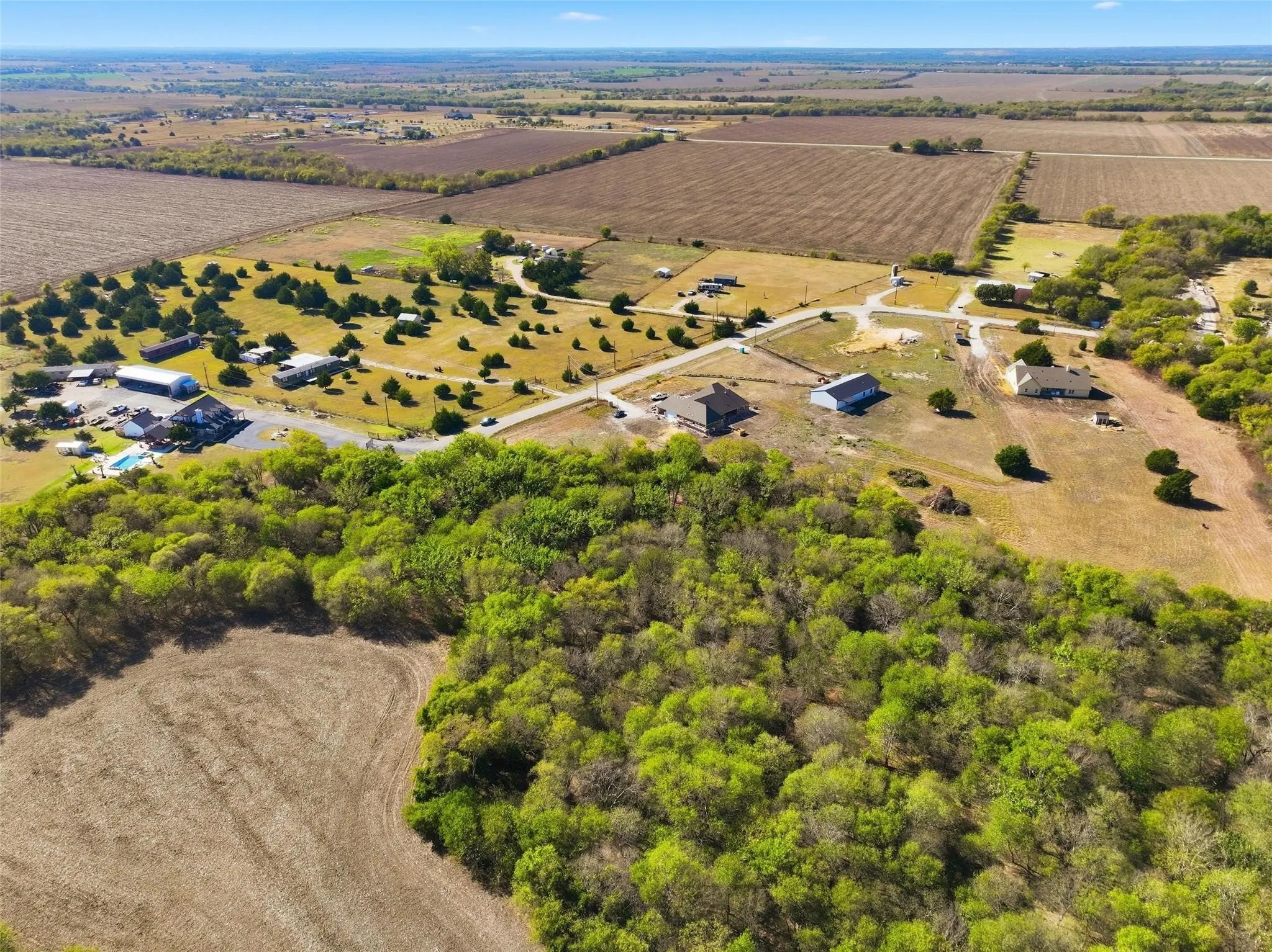 Expansive aerial landscape featuring a mix of cleared fields, wooded areas, scattered residential properties, and a visible road network