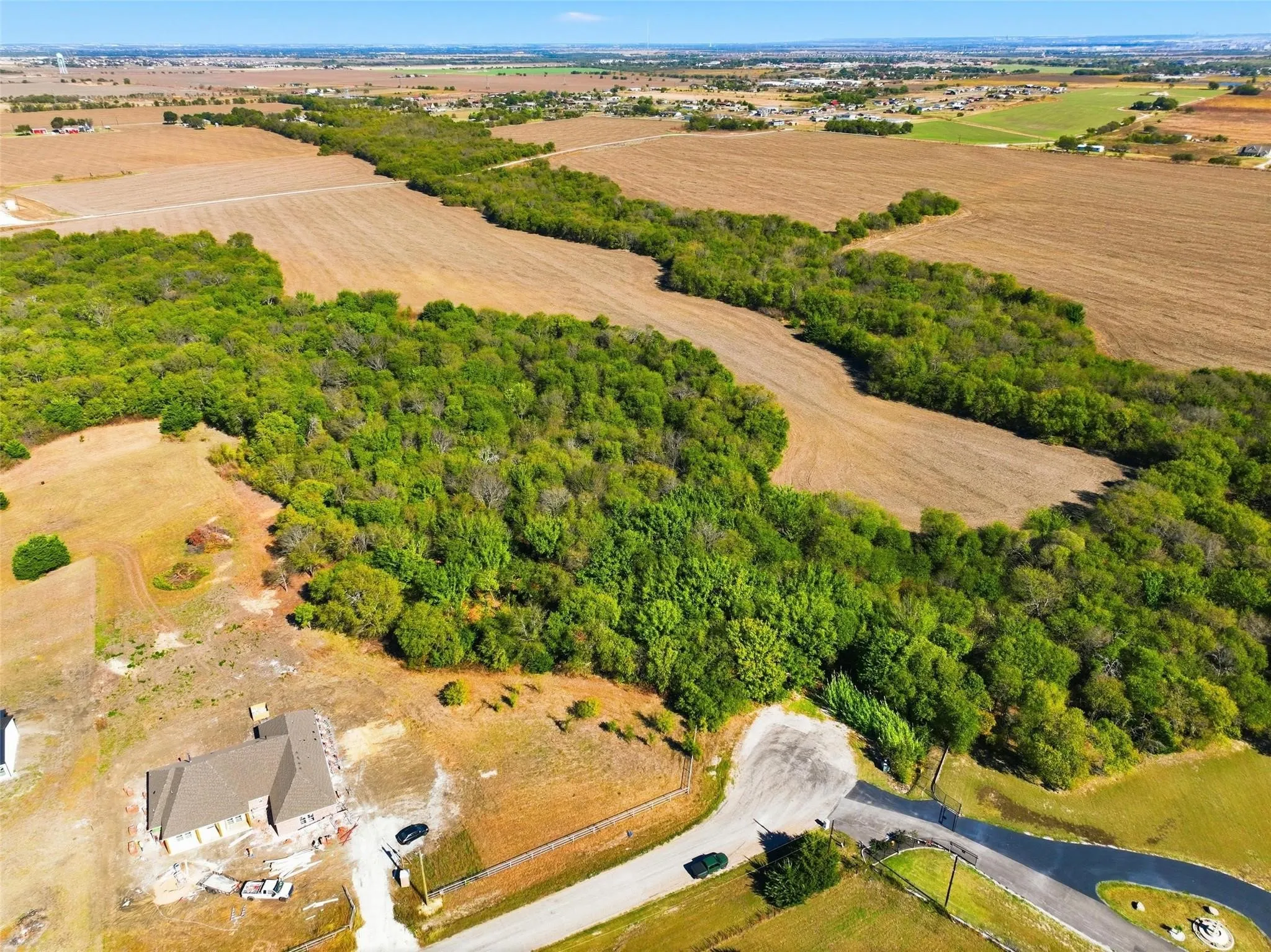 Expansive undeveloped land featuring mature tree lines and clearings, bordered by agricultural fields and distant community structures