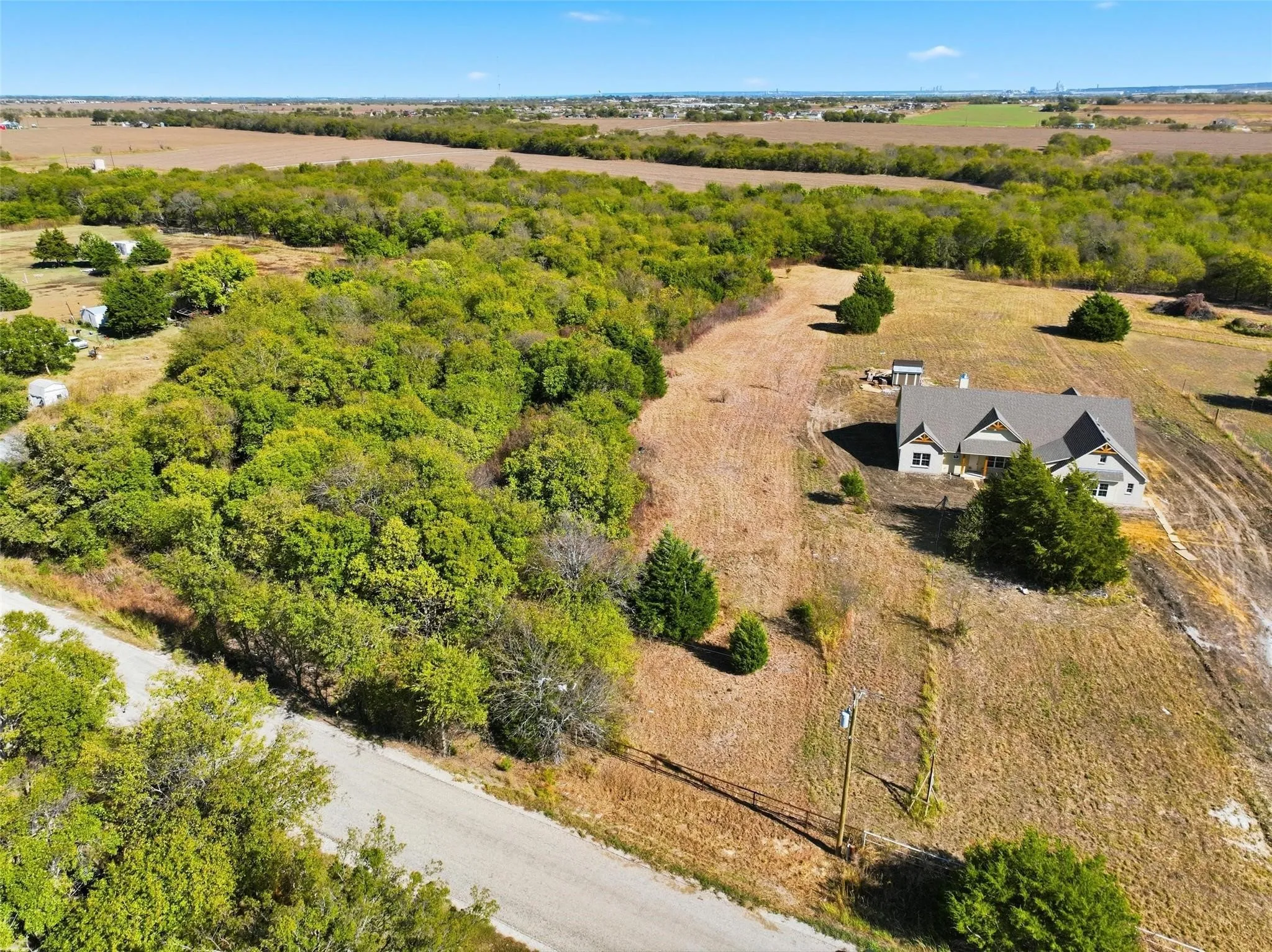 Expansive rural property featuring a newly constructed home, ample acreage, mature trees, open fields, and a paved road frontage