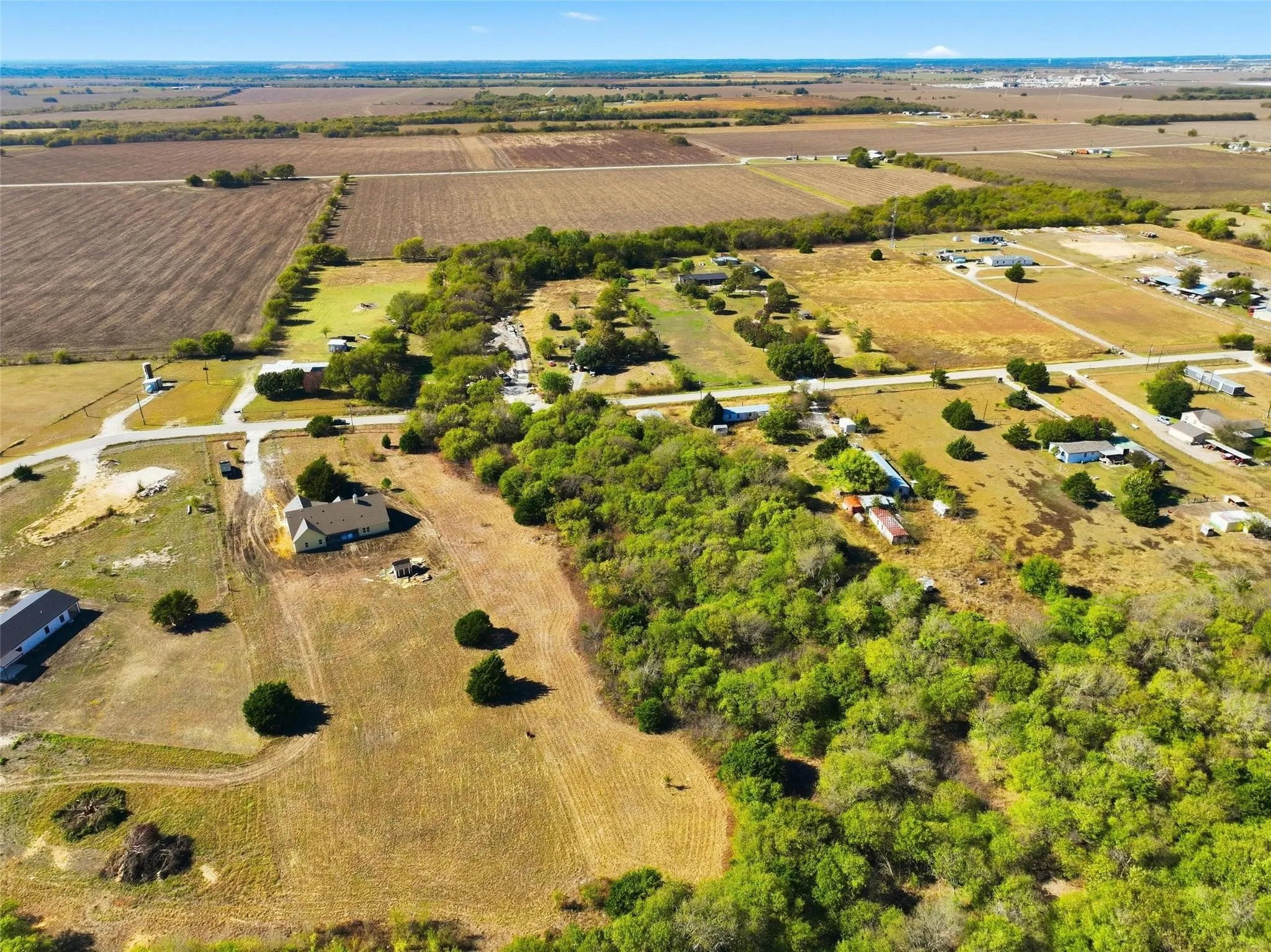 Expansive land parcel featuring open fields, natural tree lines, and paved road frontage