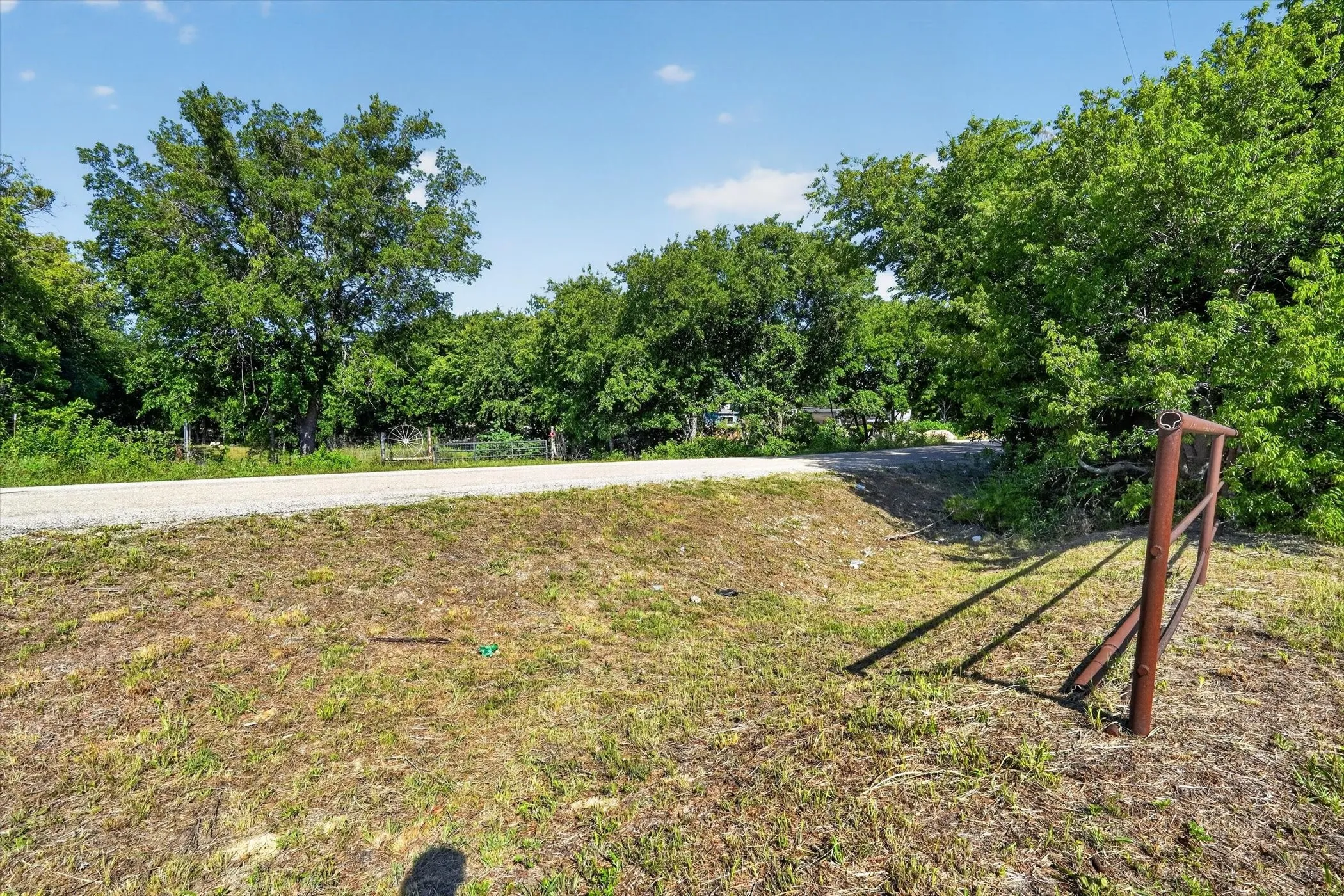 Rural land parcel with a road, mature trees, and a metal fence