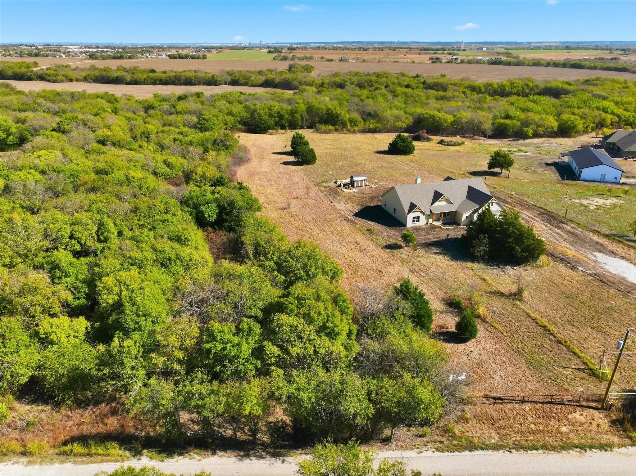 Expansive rural property featuring a single-story home with a gabled roof, surrounded by mature trees and open land