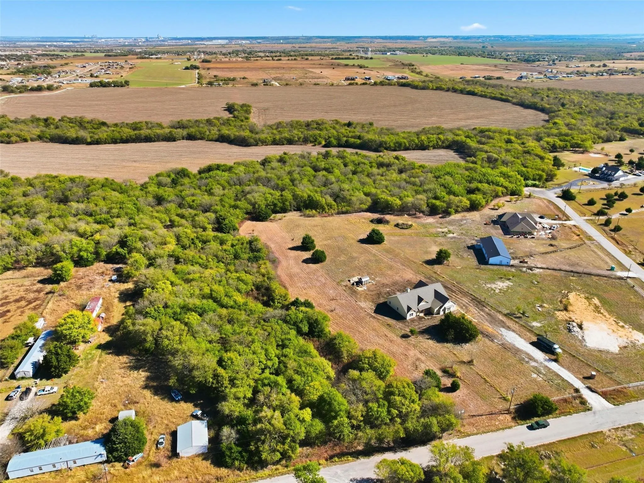 Expansive land parcel featuring open fields, natural tree lines, and paved road frontage
