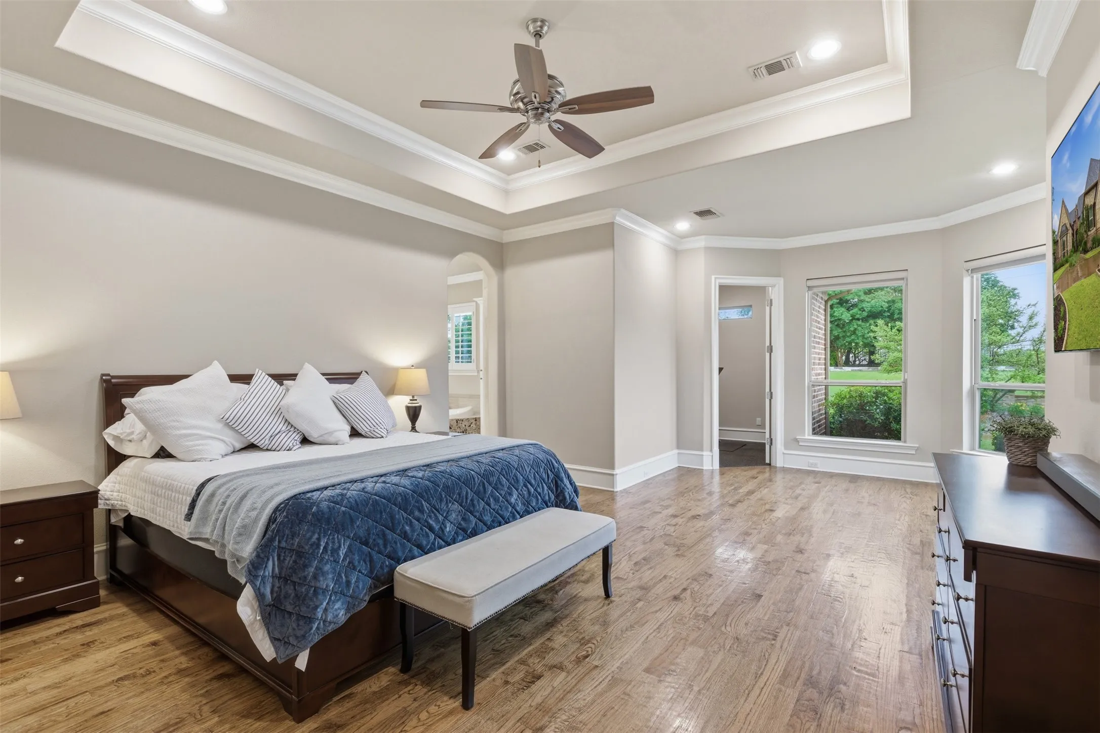 Spacious room featuring wood-finish flooring, a tray ceiling with recessed lighting, an arched doorway, and multiple windows with exterior landscaping
