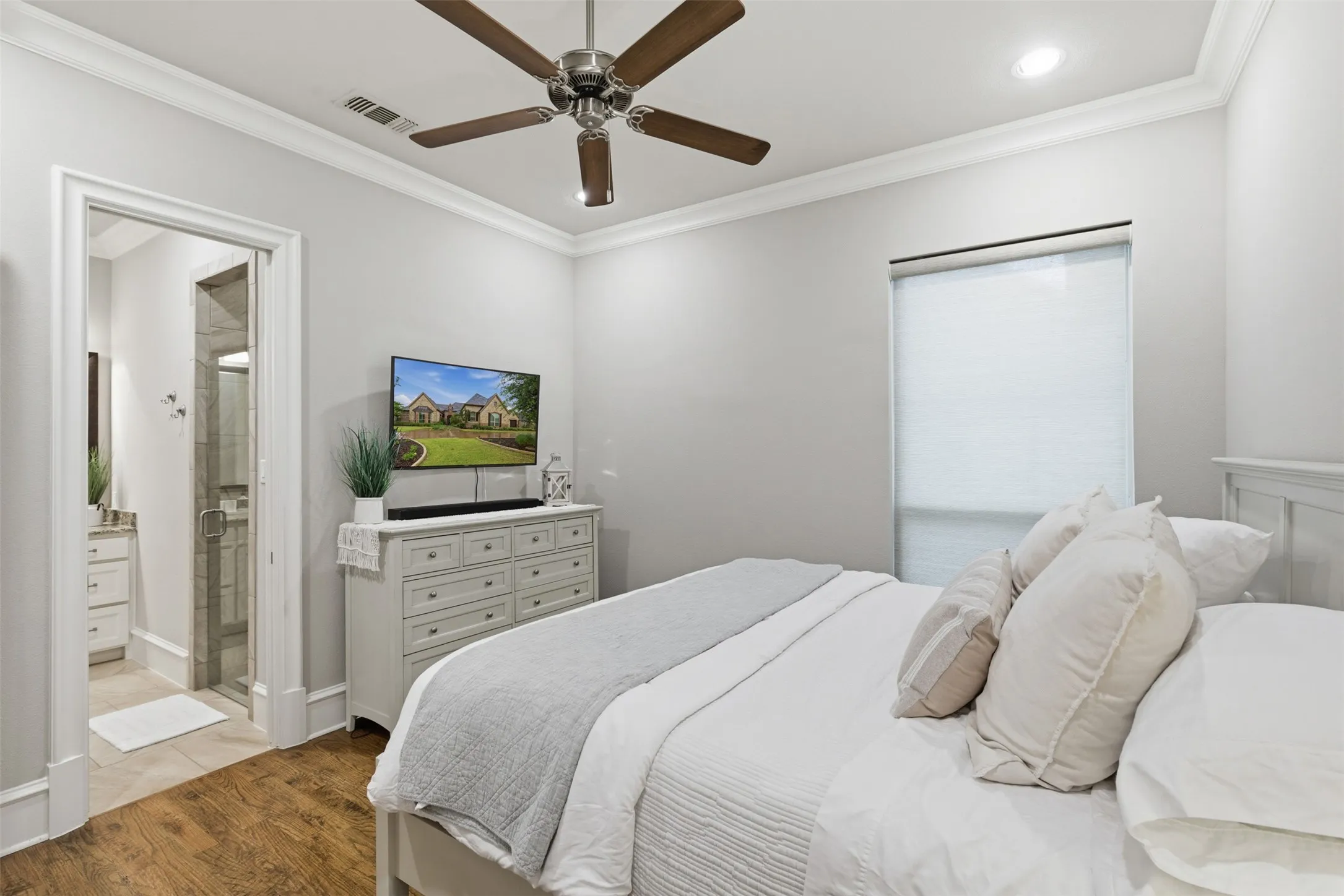 Spacious bedroom featuring wood-finish flooring, a ceiling fan with light, and crown molding