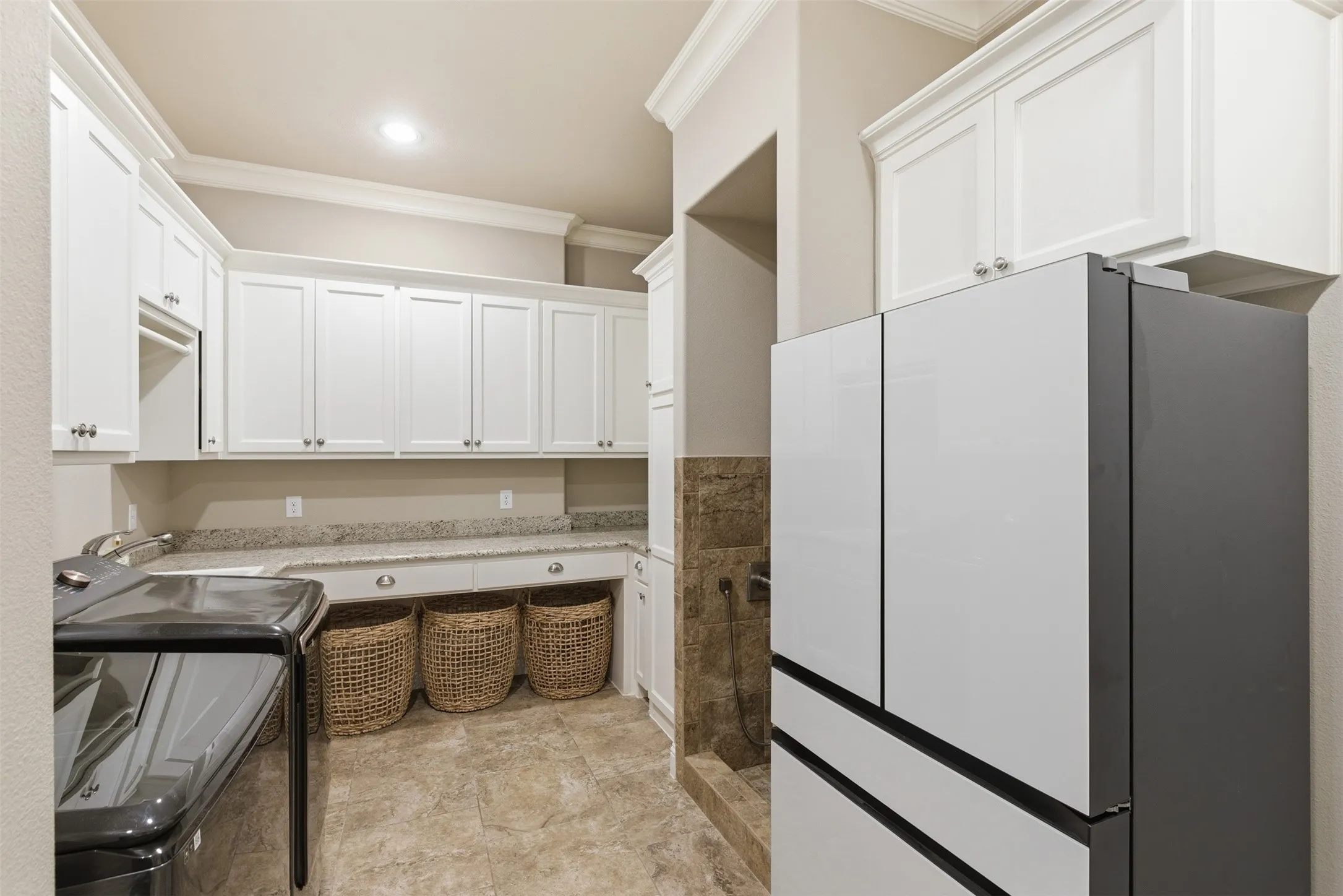Utility room featuring extensive white cabinetry, light granite-finish countertops, and tiled flooring
