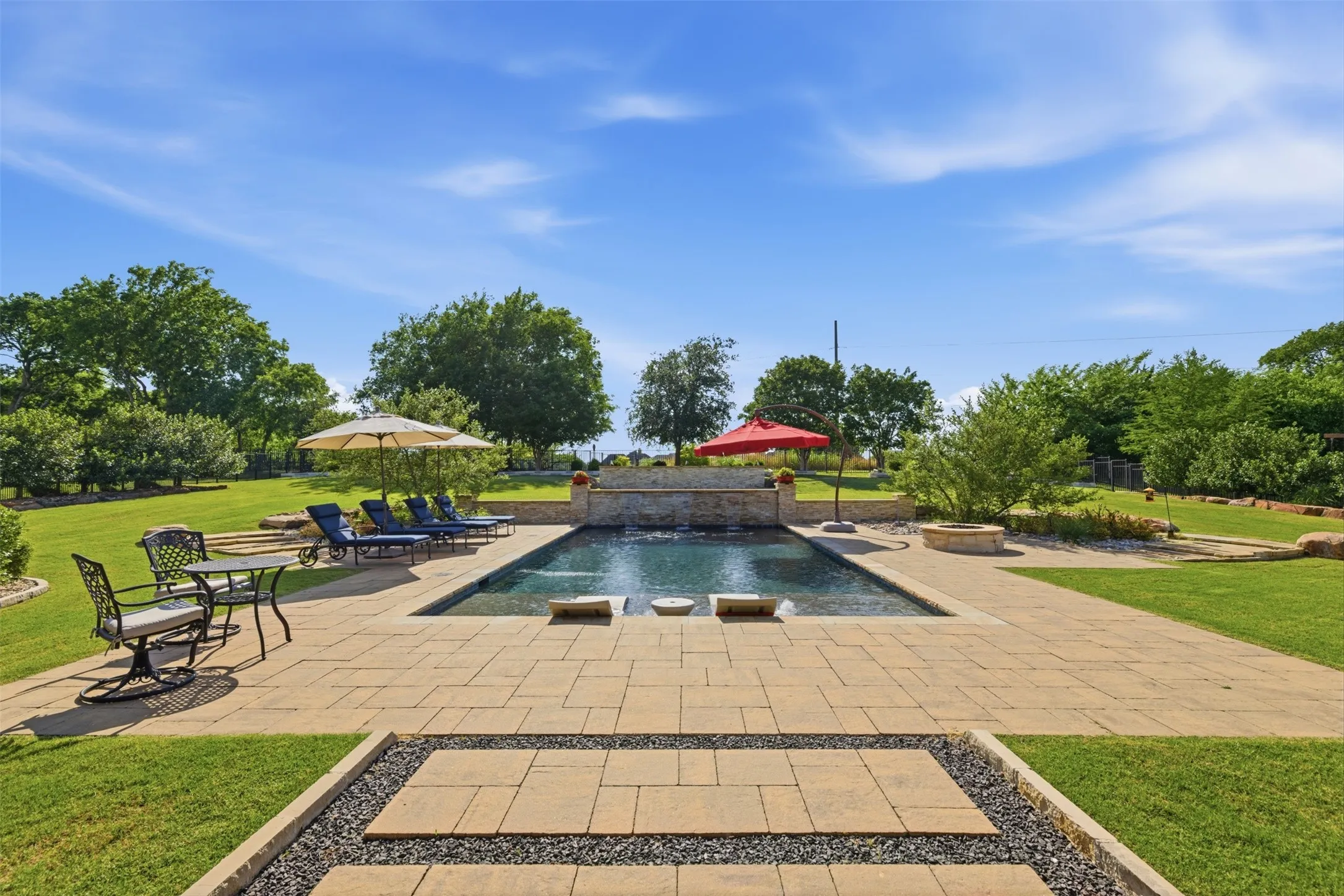 Rectangular swimming pool featuring a stone waterfall, surrounded by extensive paver decking