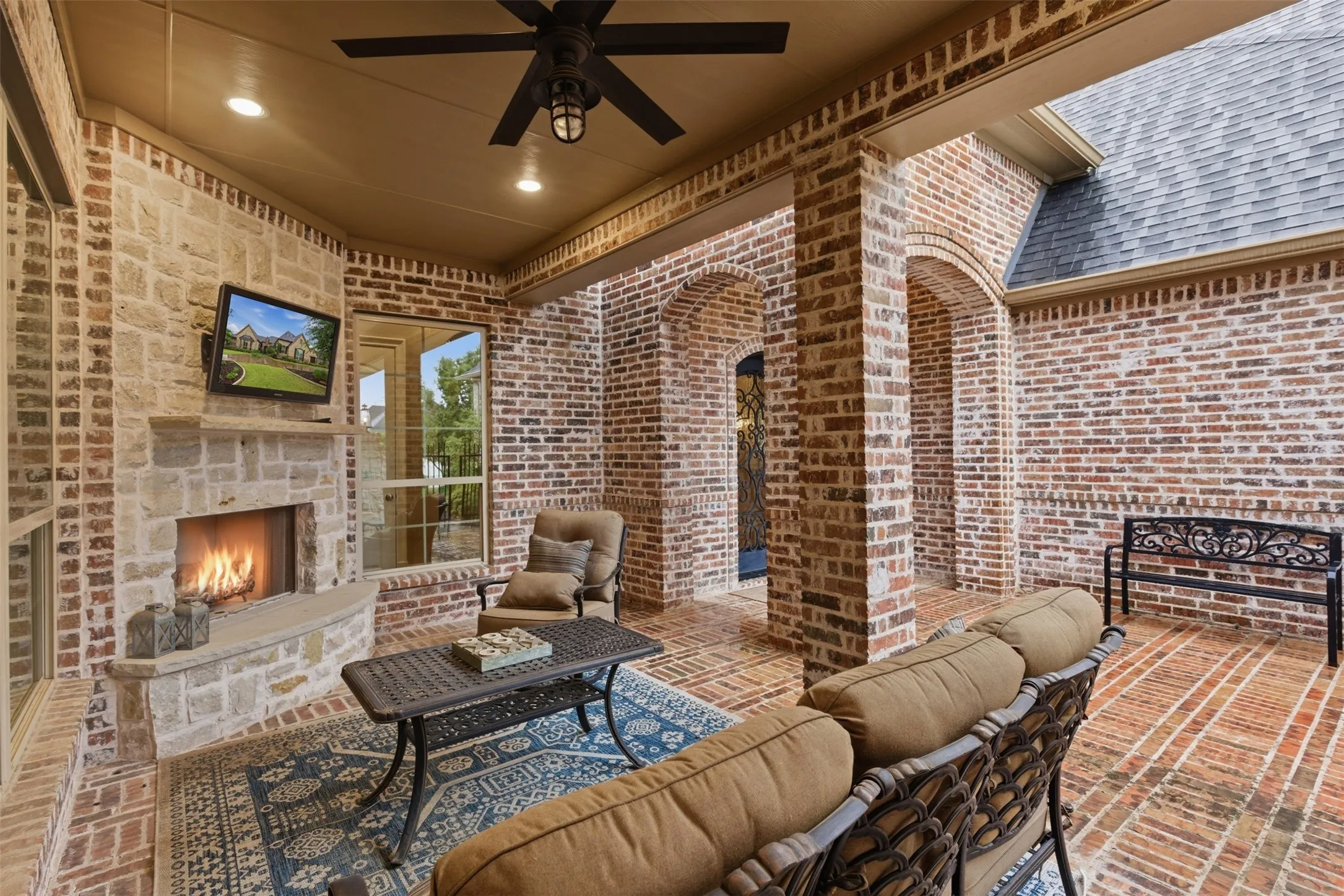 Expansive covered patio featuring a stone fireplace with hearth, brick walls, and a brick paver floor