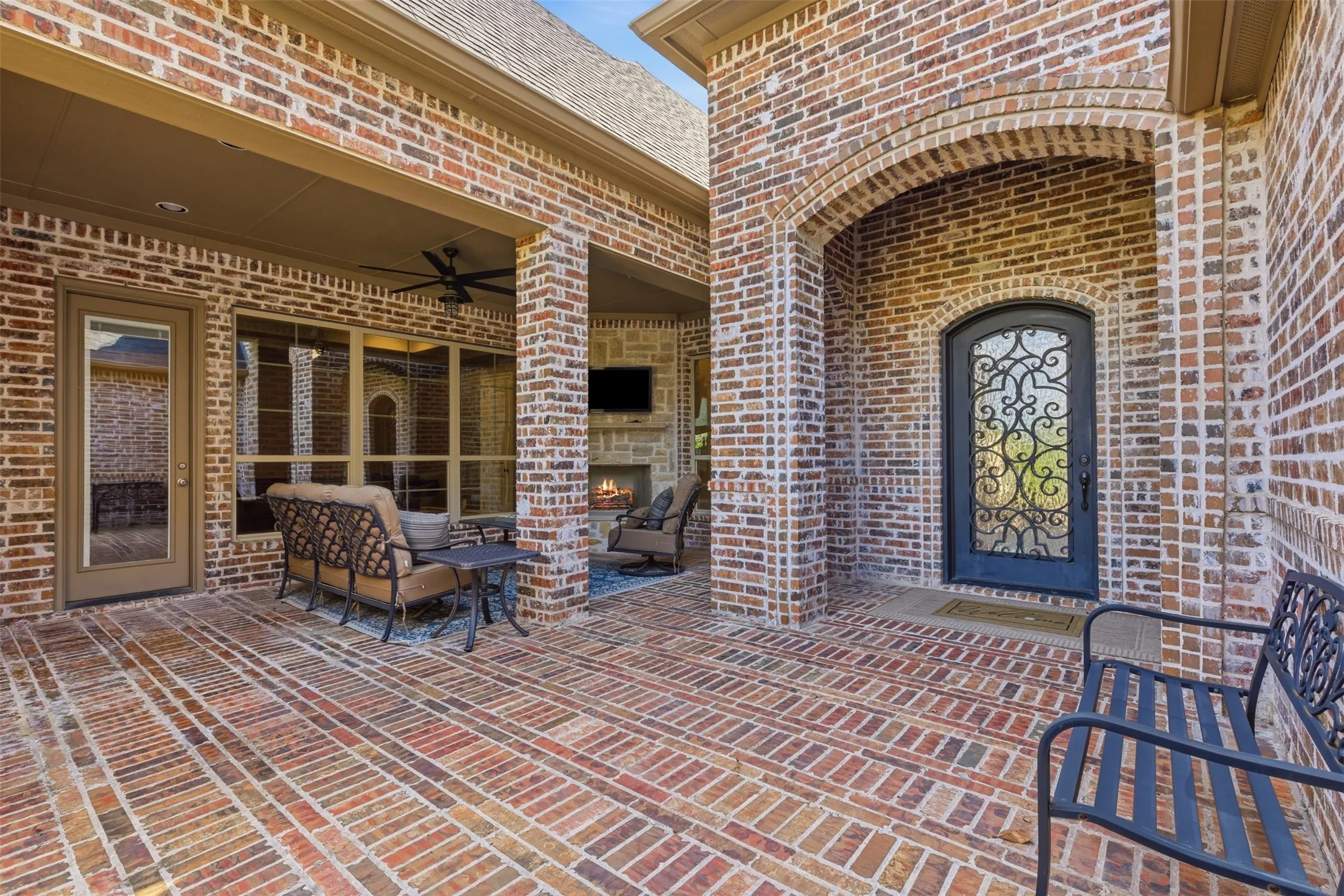 Expansive brick patio featuring a covered outdoor living area with a stone fireplace, ceiling fan, and large windows