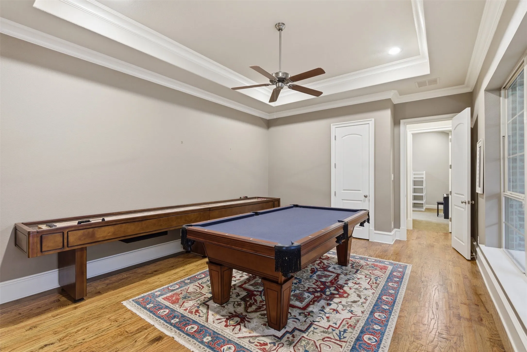 Spacious room featuring wood-finish flooring, tray ceiling with a ceiling fan, recessed lighting, and crown molding