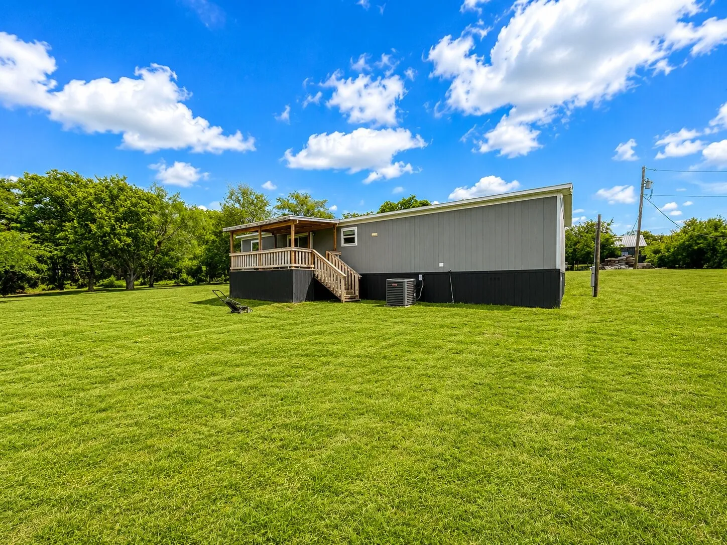 Expansive green lawn surrounds a grey-sided structure featuring a wooden deck with railing and stairs