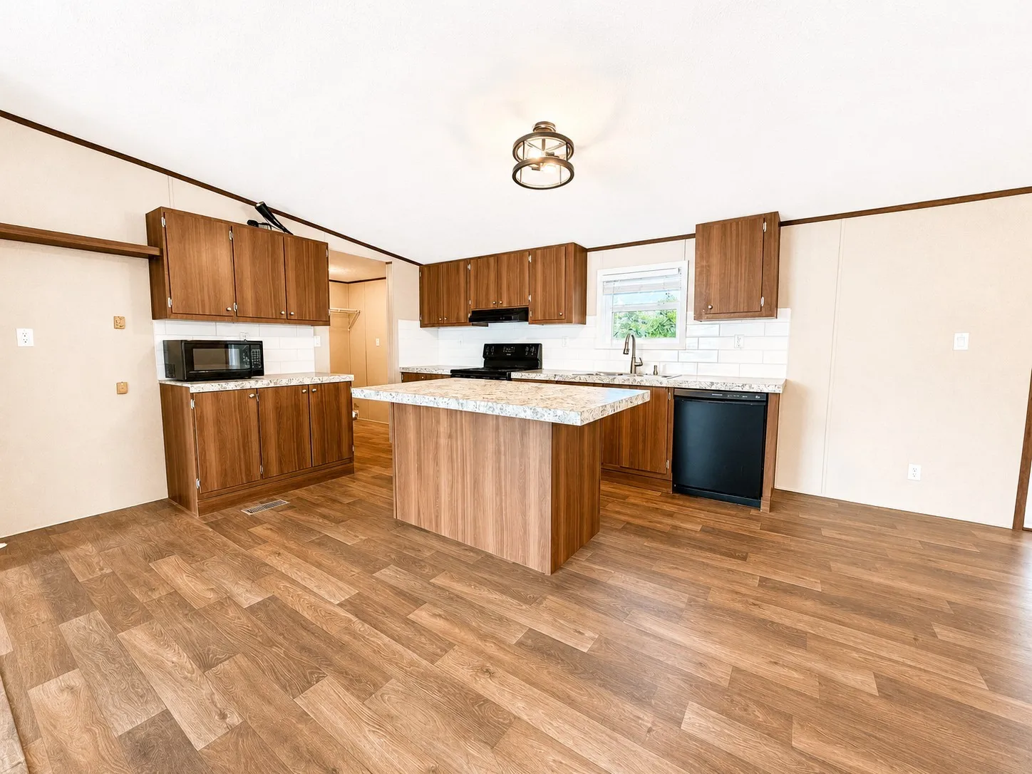 Open-concept kitchen and dining area featuring wood-finish flooring, wood cabinetry, light-toned granite-style countertops, and a subway tile backsplash