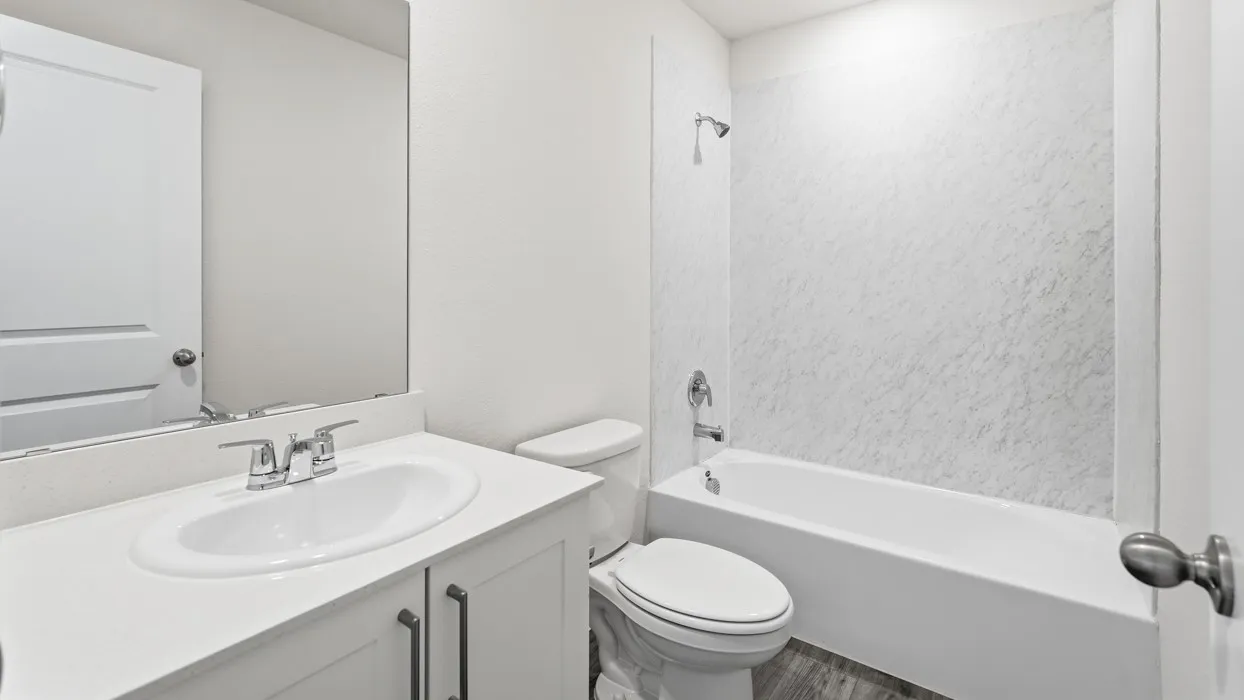 Bathroom featuring a white tub with textured surround, a white vanity with an integrated sink, polished chrome faucet, and wood-finish flooring