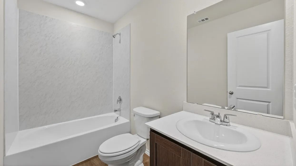 Bathroom featuring a white bathtub with a textured shower surround, a white toilet, and a vanity with a white countertop and integrated sink