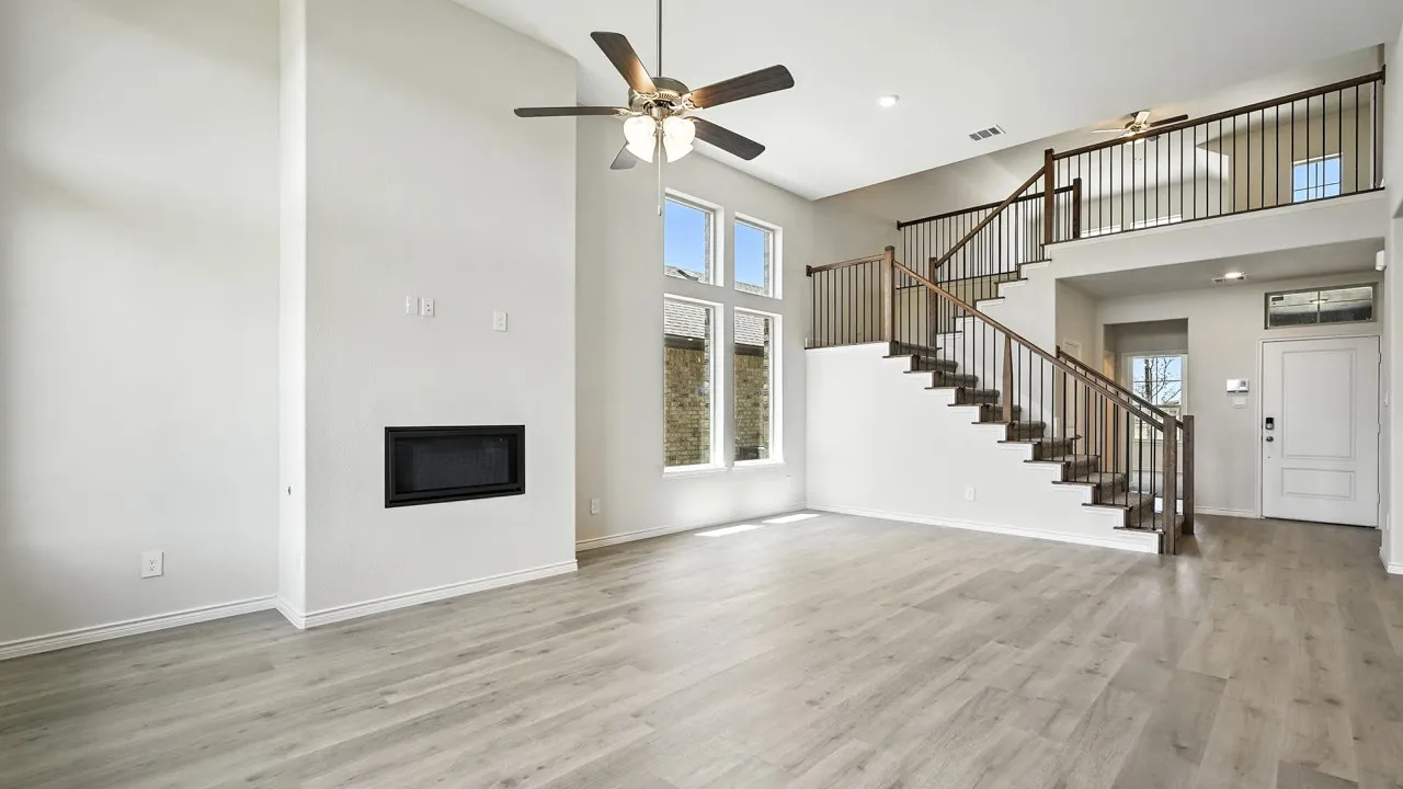 Two-story living area featuring a built-in fireplace, wood-finish flooring, a contemporary ceiling fan, and a prominent staircase with dark wood handrails and black metal balusters