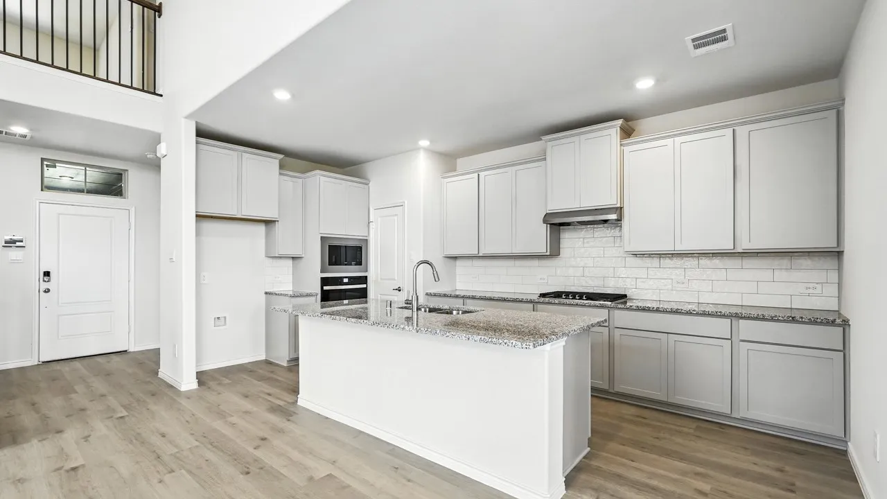 Contemporary kitchen featuring an island with a sink, stainless steel appliances, light gray cabinetry, subway tile backsplash, and wood-finish flooring