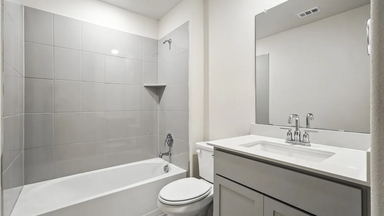 Bathroom featuring a built-in tub with light grey subway tile surround, a built-in shower niche, a vanity with a white countertop and integrated sink, and a chrome faucet