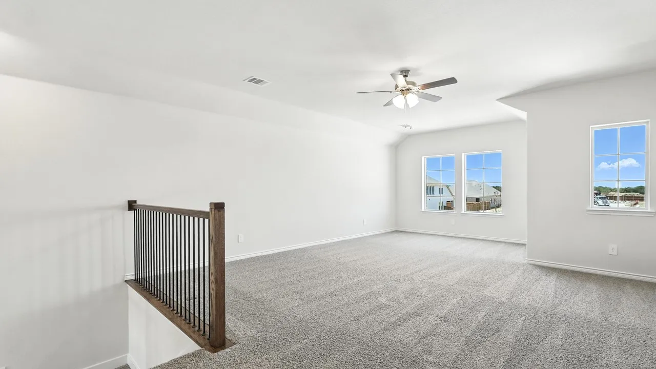 Spacious carpeted room featuring a ceiling fan, three windows, and a wood and metal railing overlooking a lower level