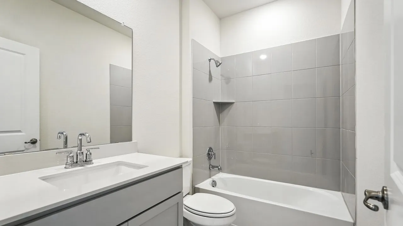 Bathroom featuring a single vanity with an integrated sink, polished chrome faucet, a large frameless mirror, and a tub-shower combination with gray subway tile surround and a built-in shower niche