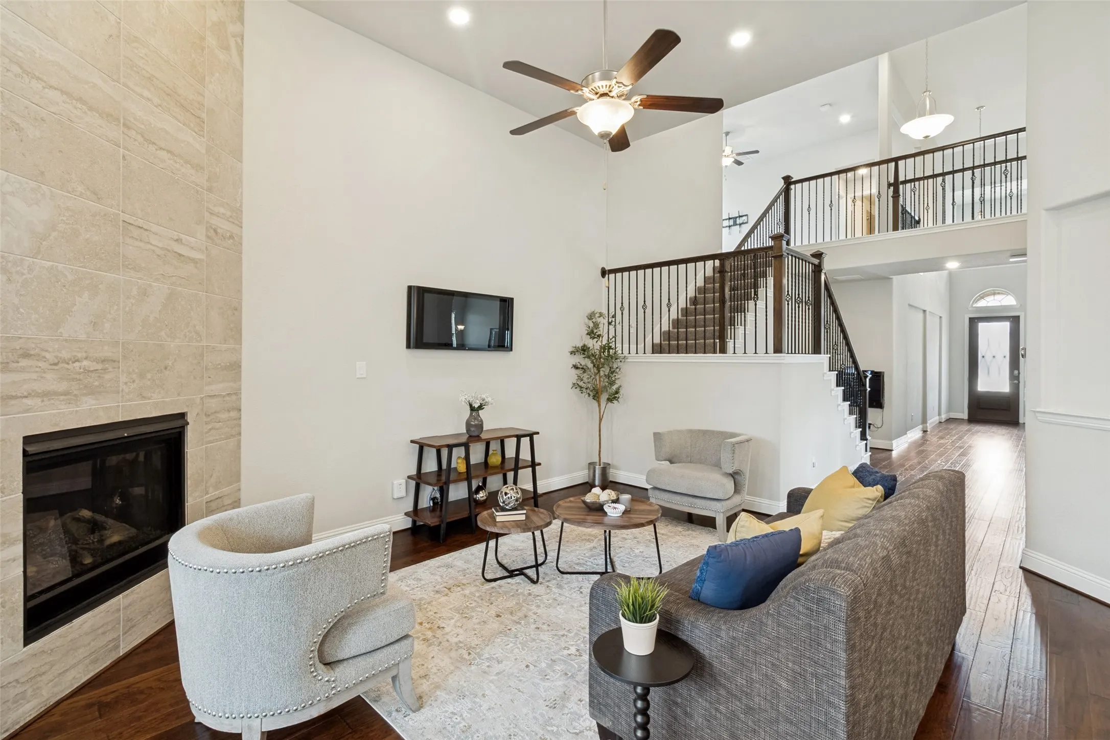 Living area featuring a two-story ceiling, wood-finish flooring, and a fireplace with a stone-tiled surround