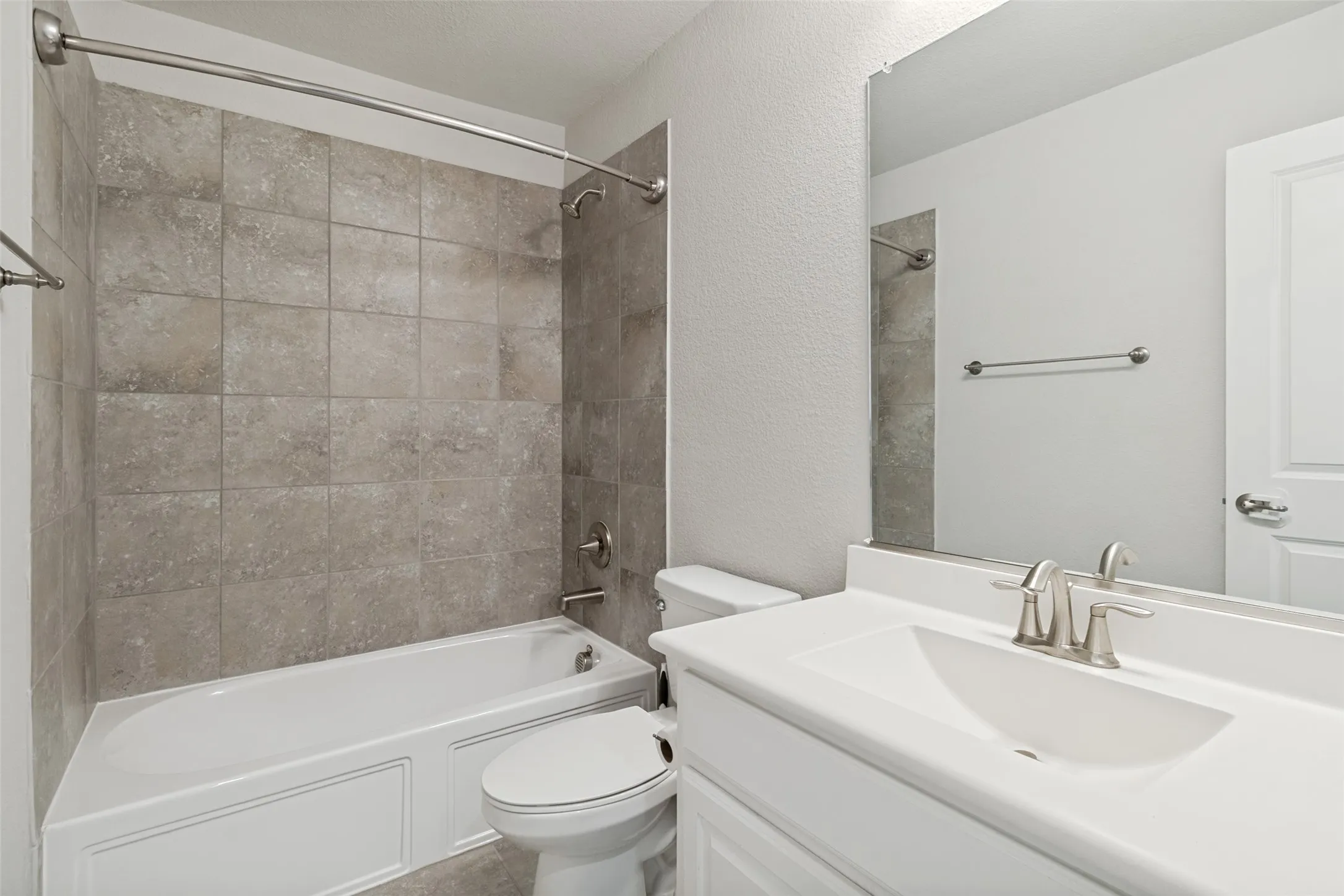 Full bathroom featuring a white tub with subway tile surround, a white vanity with integrated sink, and a large wall-mounted mirror