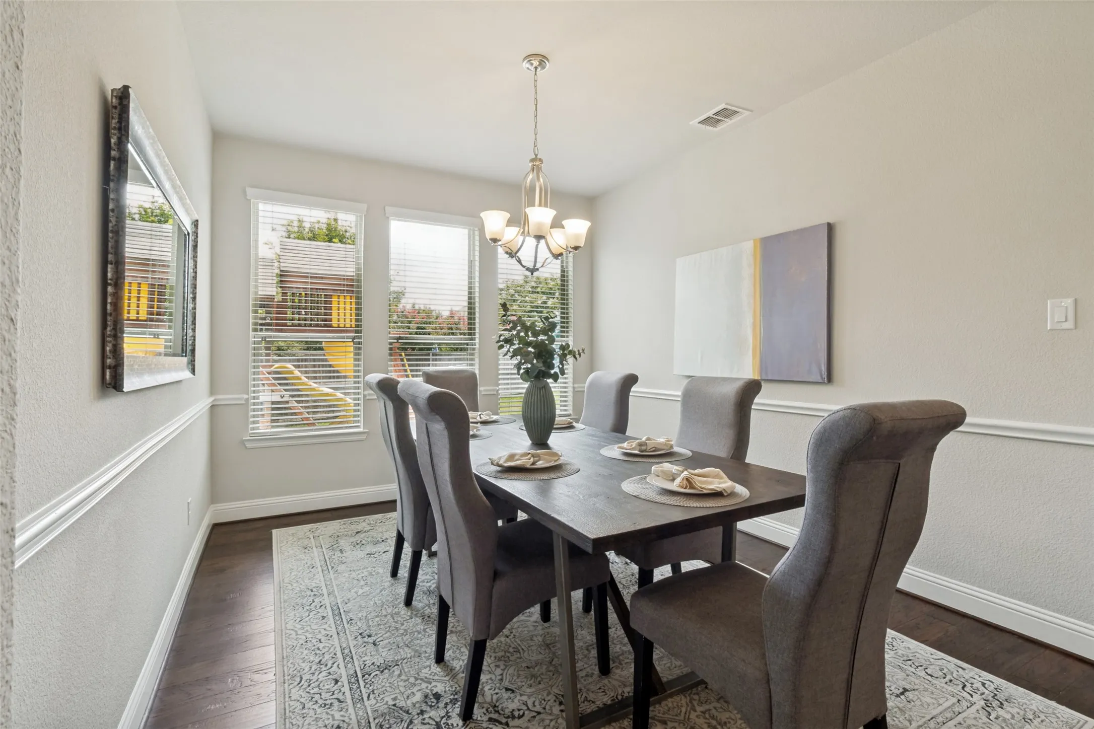 Dining area featuring wood-finish flooring, multiple windows with blinds, a chandelier light fixture, and wainscoting