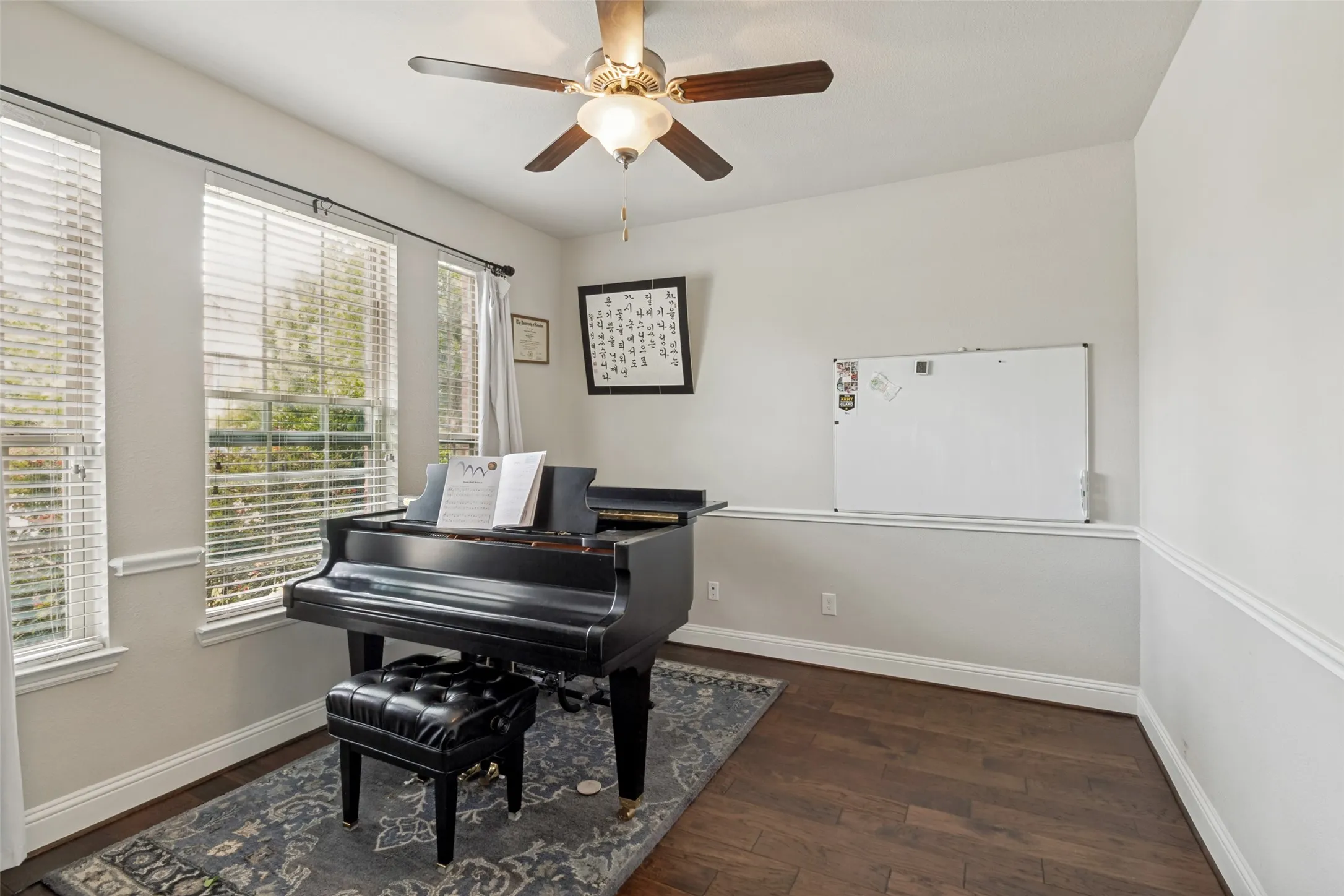 Bright room featuring wood-finish flooring, multiple windows with blinds, a ceiling fan with integrated lighting, and chair rail molding