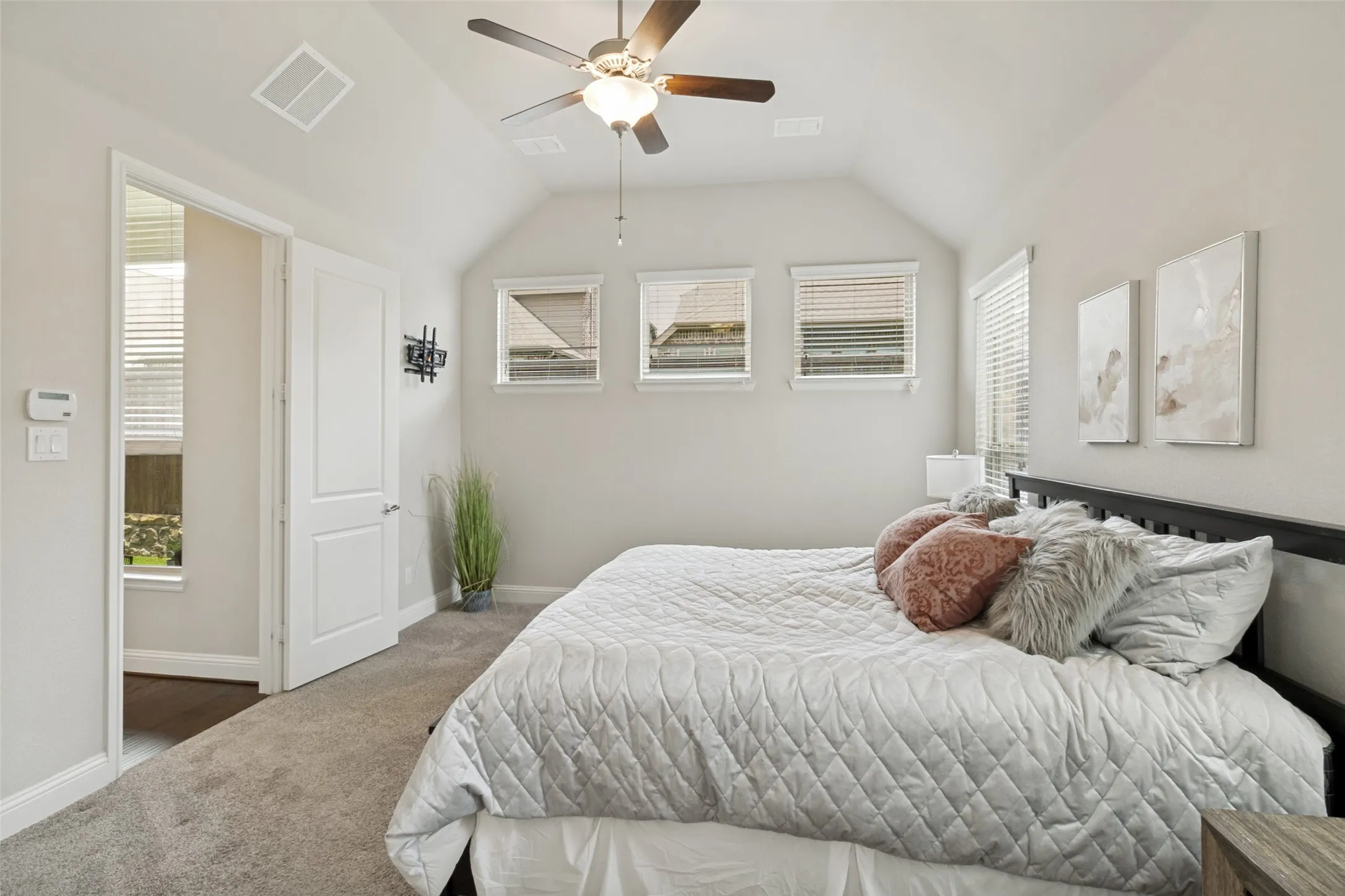Carpeted interior room featuring vaulted ceilings, a ceiling fan with integrated lighting, and multiple windows