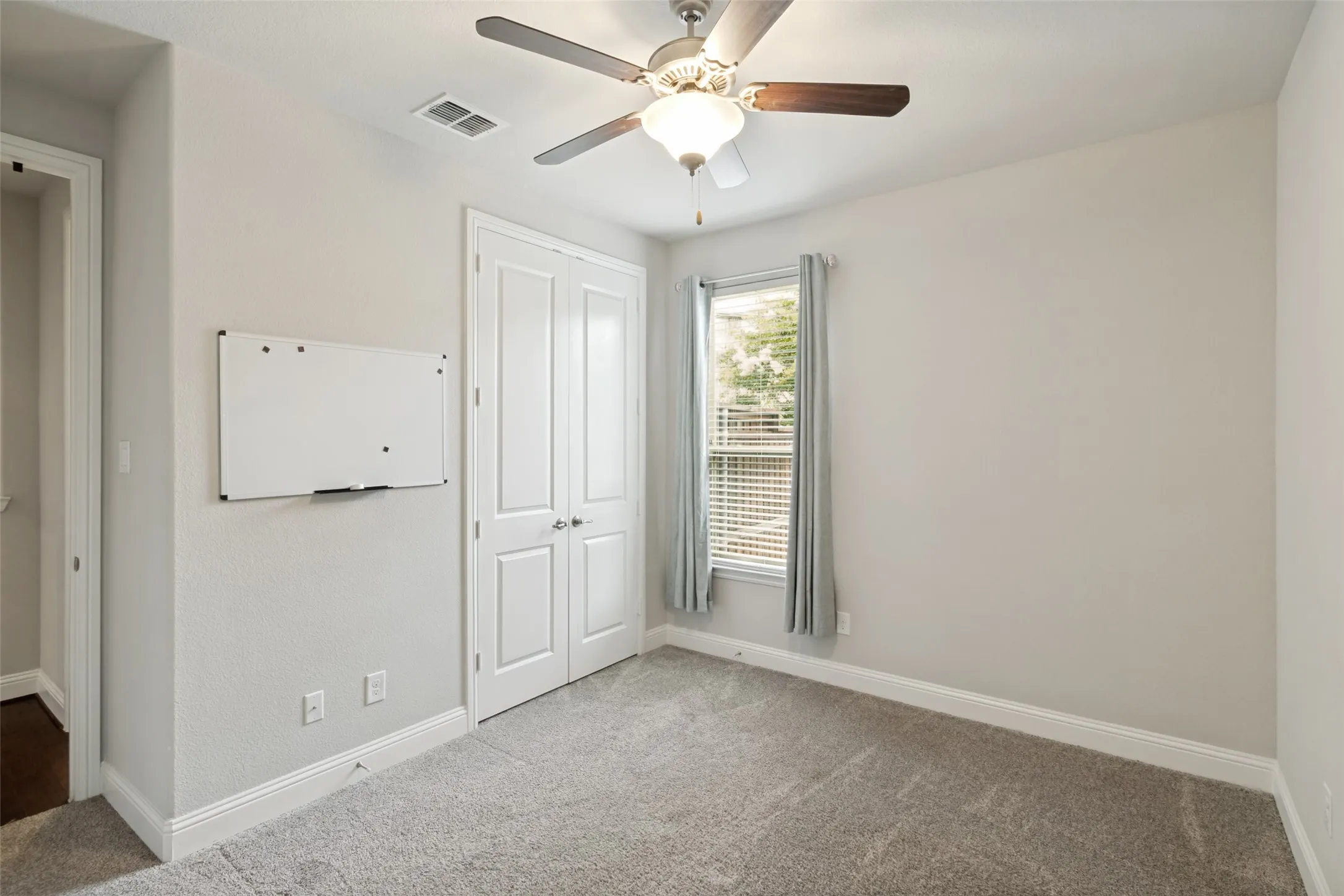 Carpeted room with a ceiling fan light fixture, double-door closet, and a single window with blinds and drapes