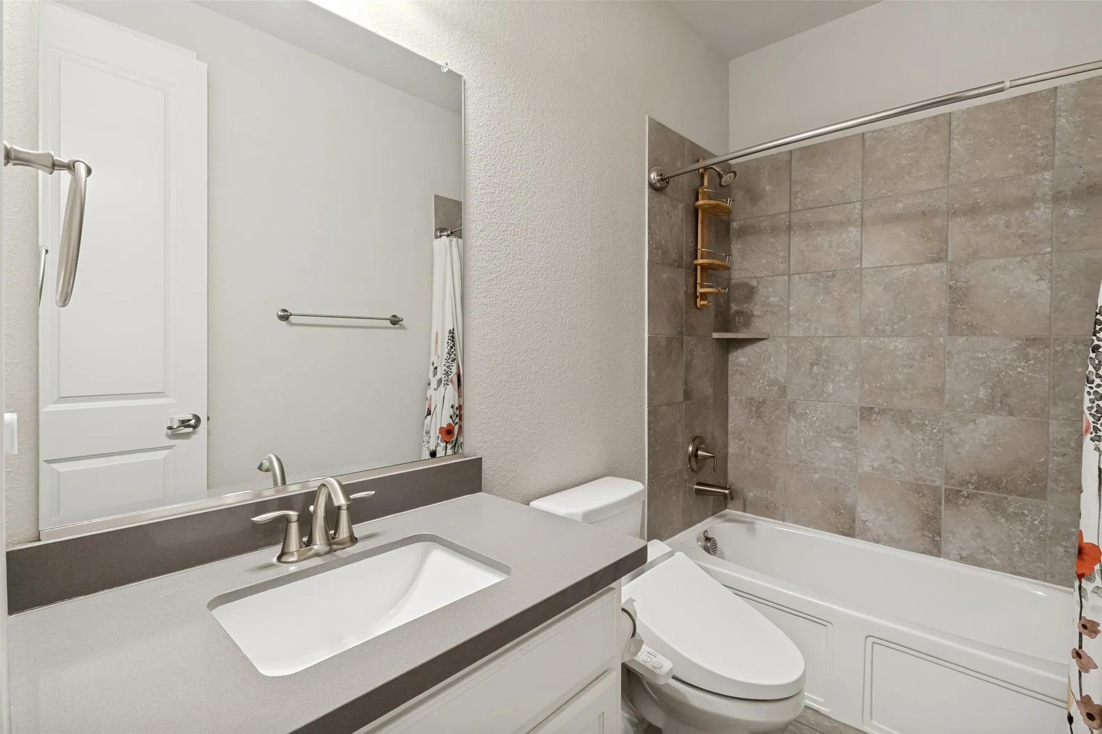 Bathroom featuring a single vanity with a rectangular sink and gray countertop, brushed nickel faucet, large wall mirror, and a tub/shower combination with tile surround