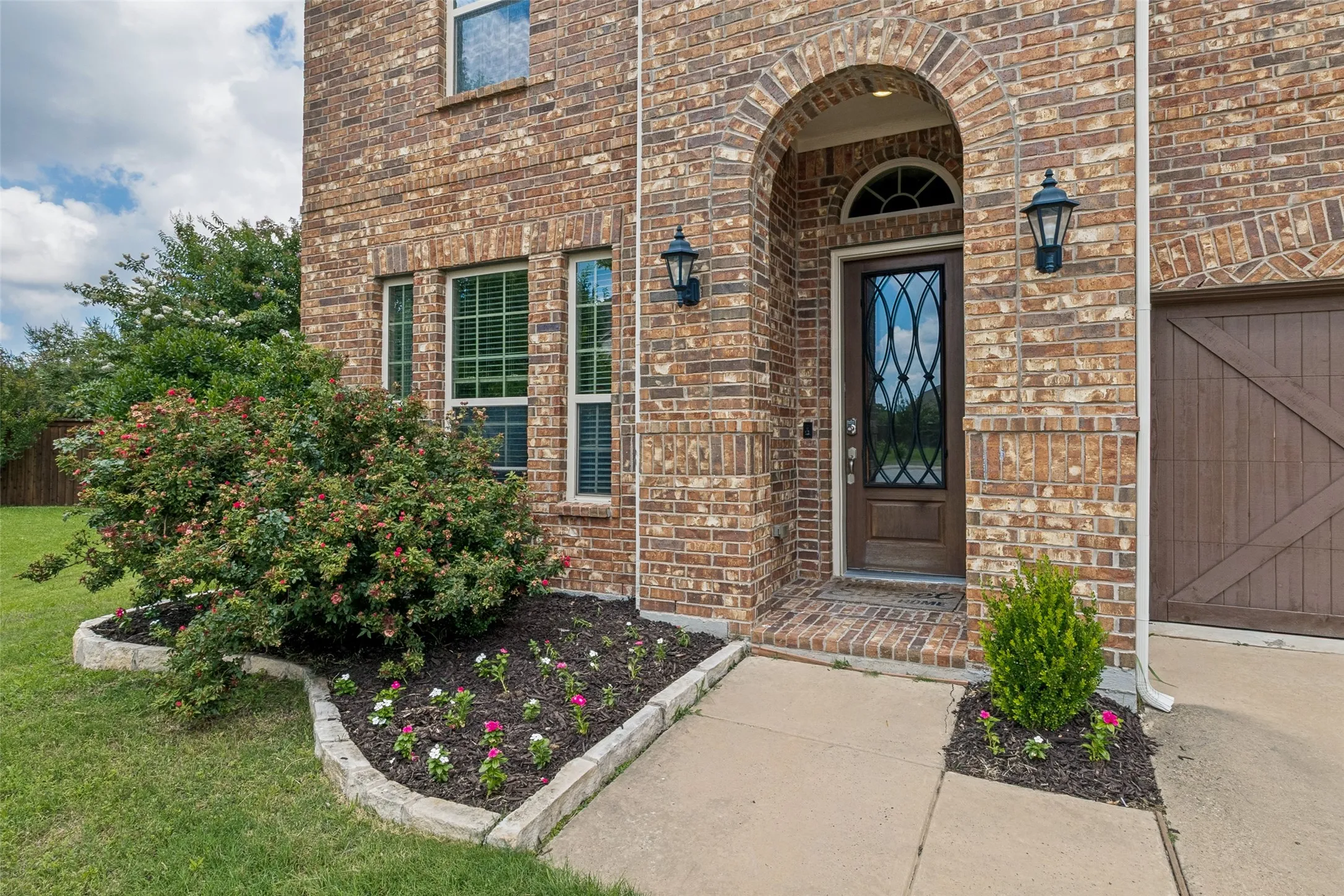 Brick façade home featuring an arched entryway with decorative glass door, exterior lighting fixtures, and a concrete walkway