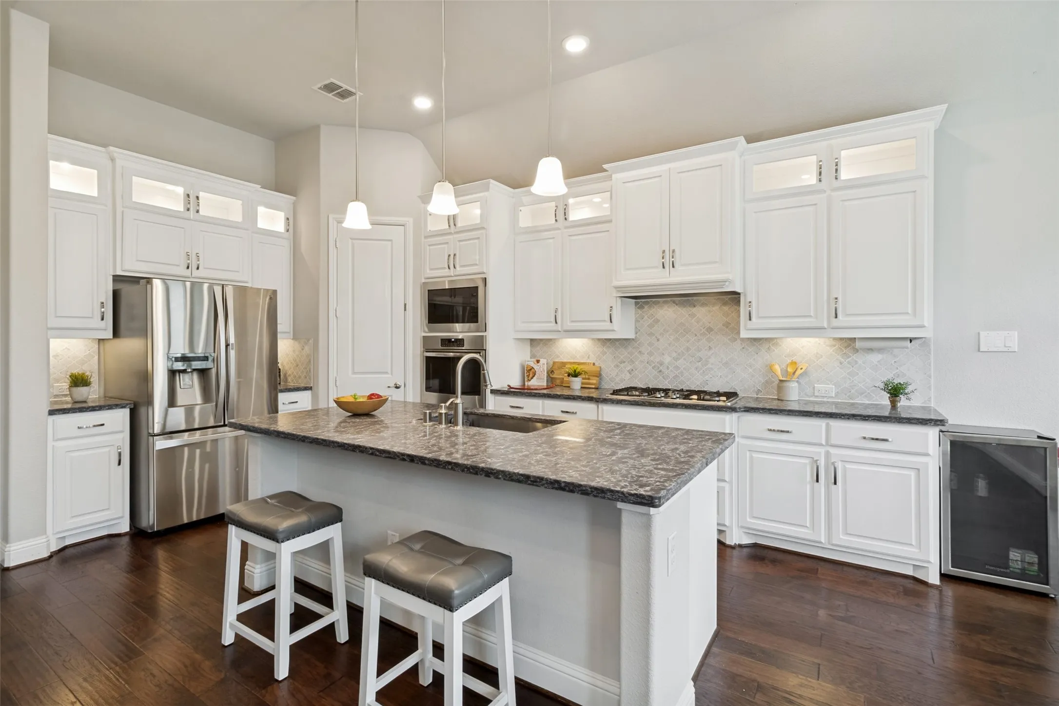 Kitchen featuring a central island with countertop seating, white shaker cabinetry, stainless steel appliances, a decorative tile backsplash, and dark wood-finish flooring