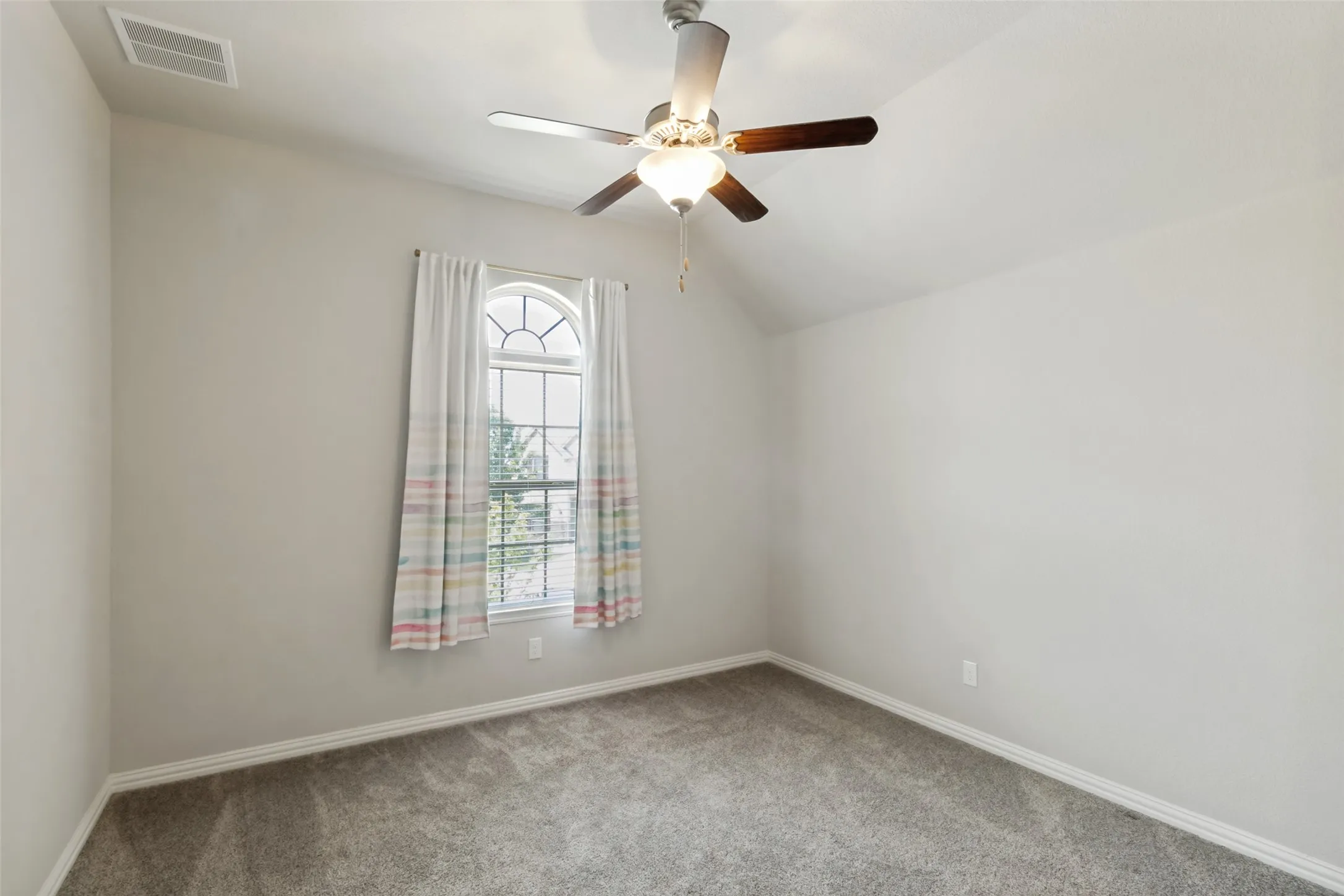 Vaulted ceiling bedroom featuring a ceiling fan with light fixture, arched window, grey carpet, and white baseboards
