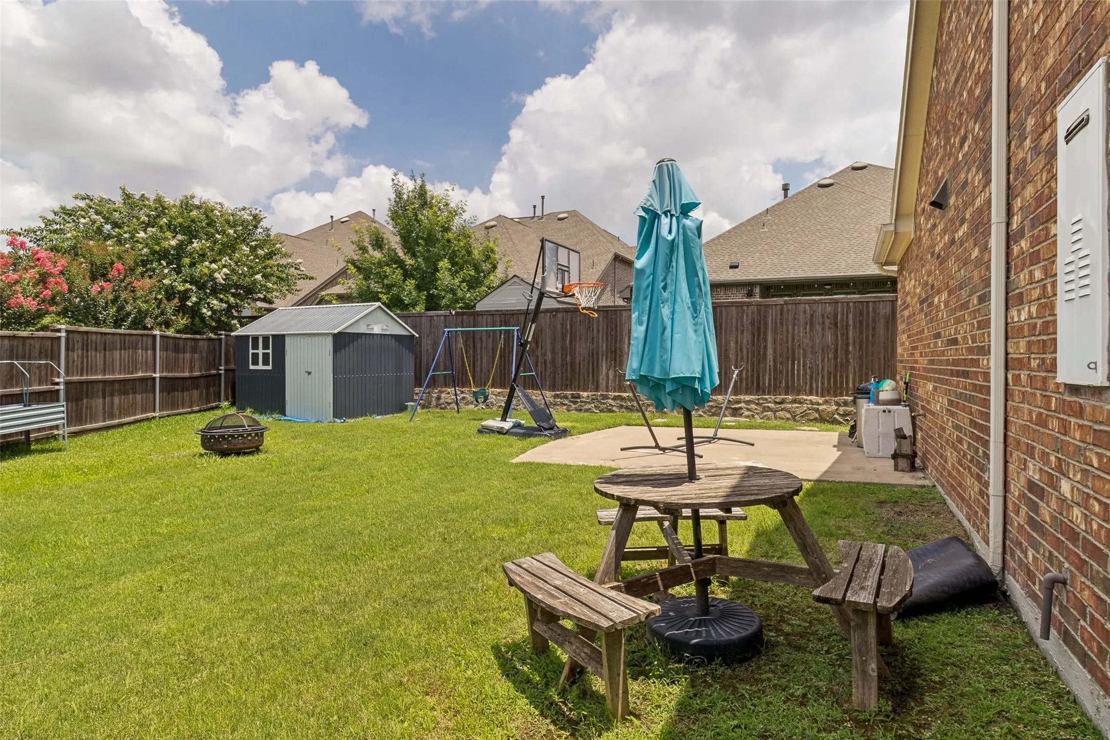 Expansive backyard featuring a manicured lawn, a detached storage shed, privacy fencing, a concrete patio, and brick exterior