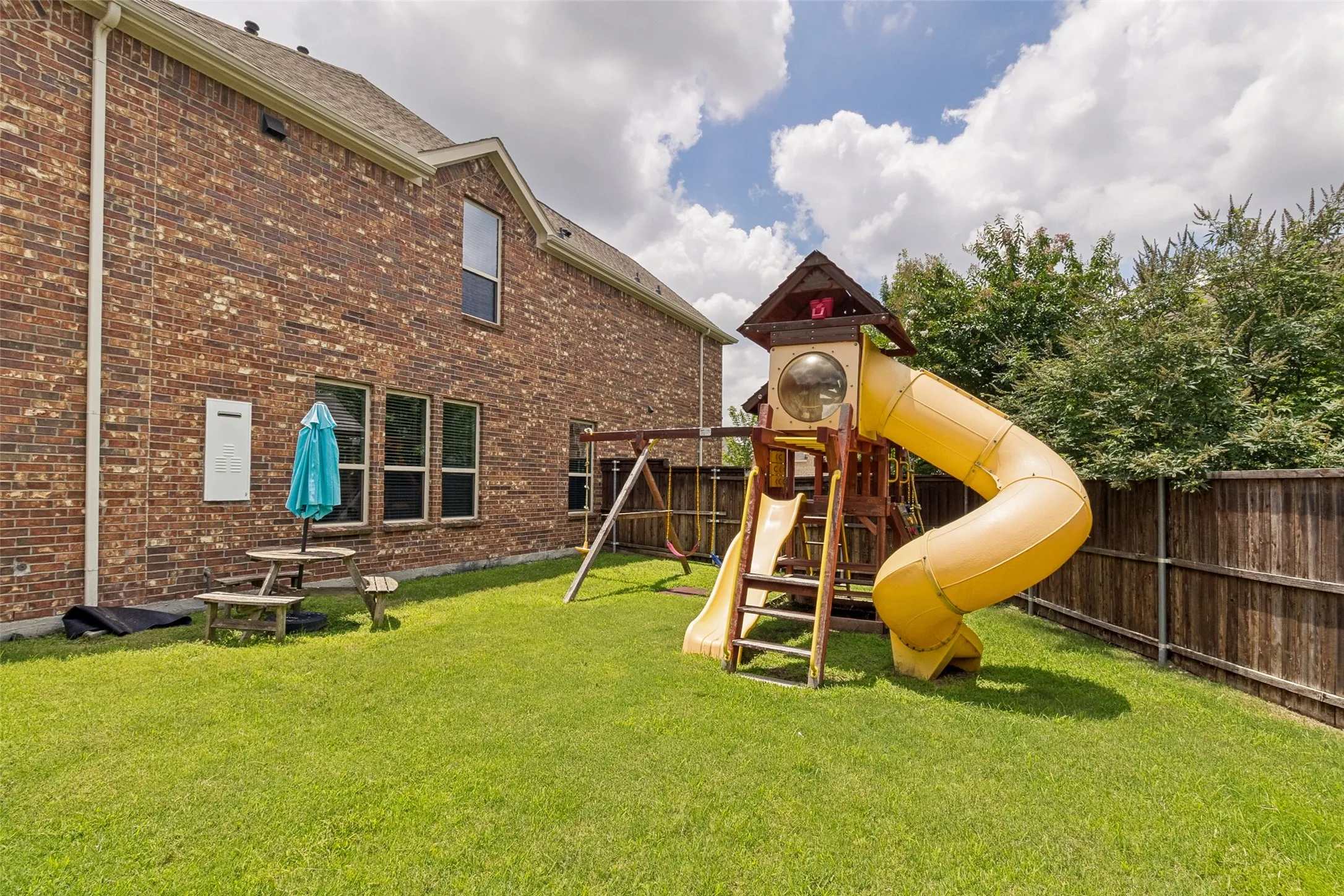 Expansive backyard featuring a lush lawn, a wooden play structure with a yellow slide, and a wooden privacy fence
