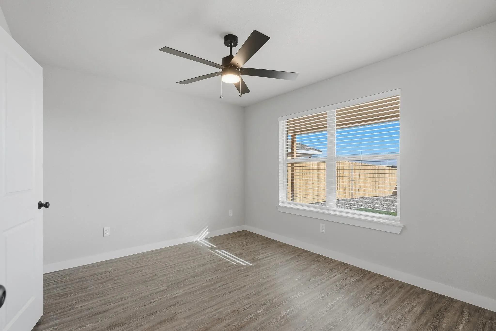 Modern interior space featuring wood-finish flooring, a contemporary ceiling fan with integrated lighting, and a window with horizontal blinds