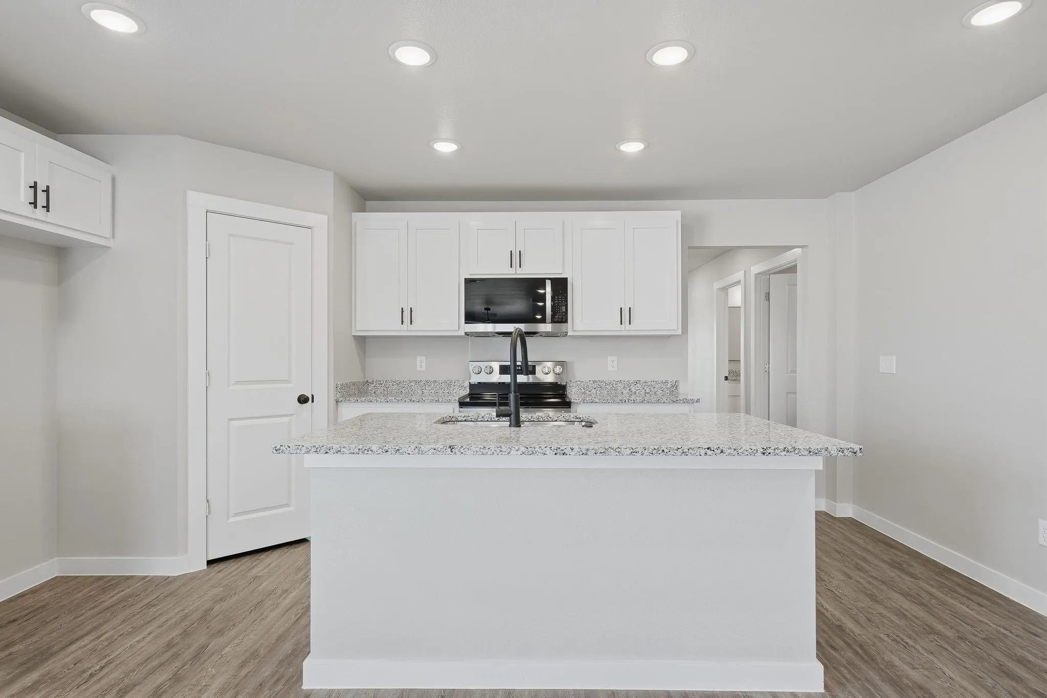 Kitchen featuring a central island with a sink, white cabinetry, integrated microwave, and speckled countertops